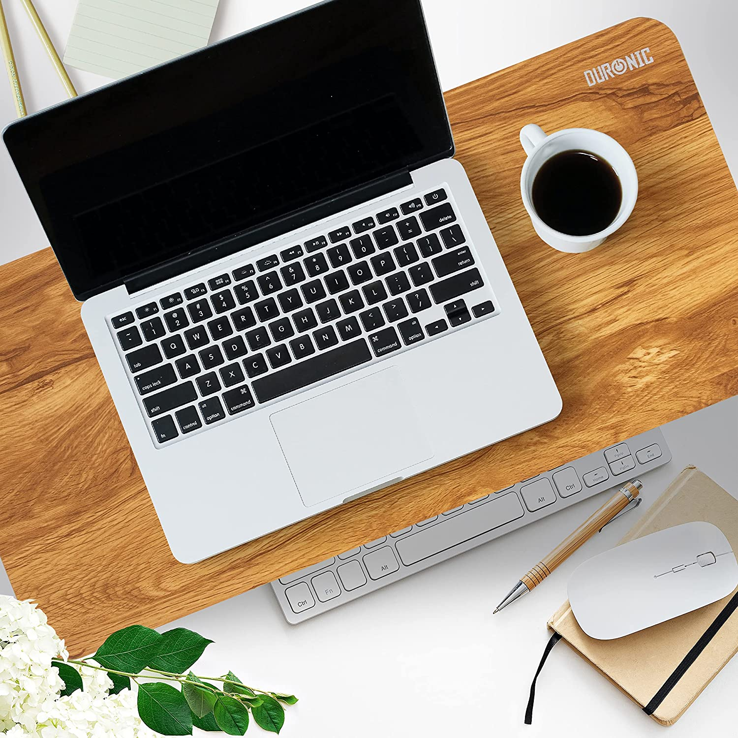 Ein Laptop auf einem Holzschreibtisch mit Tastatur, Maus, einer Tasse Kaffee und einem Notizblock.
