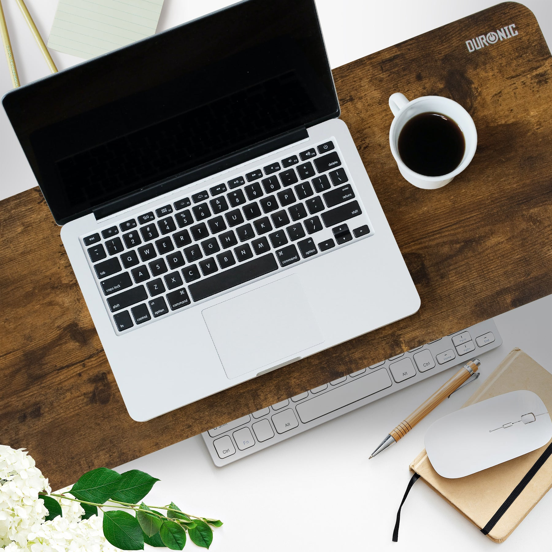 Laptop auf einem Schreibtisch mit Kaffee, Tastatur und Stift. Blumen im Vordergrund.