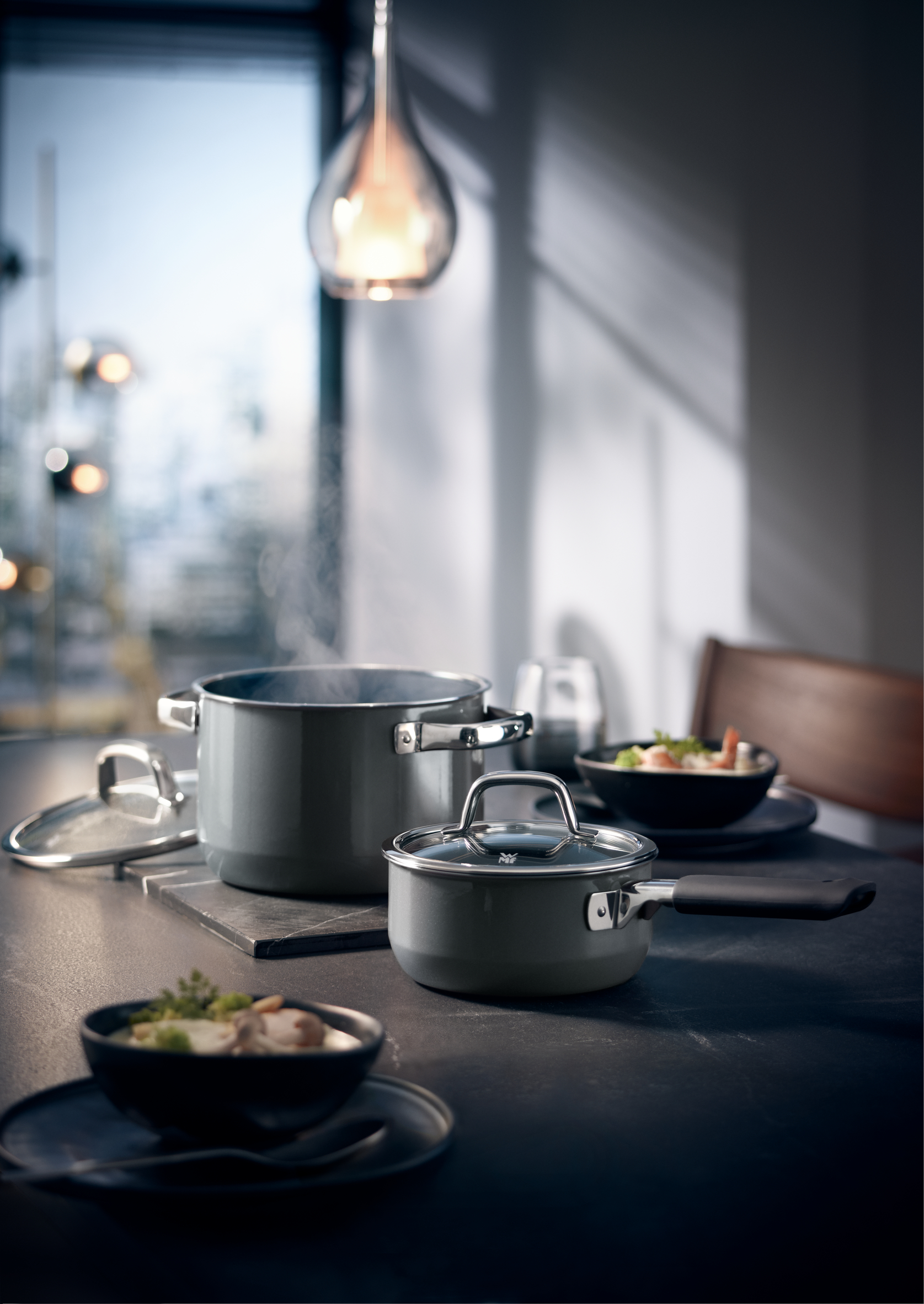 Töpfe und Schalen mit Essen auf einem Tisch. Eine beleuchtete Lampe über dem Tisch.