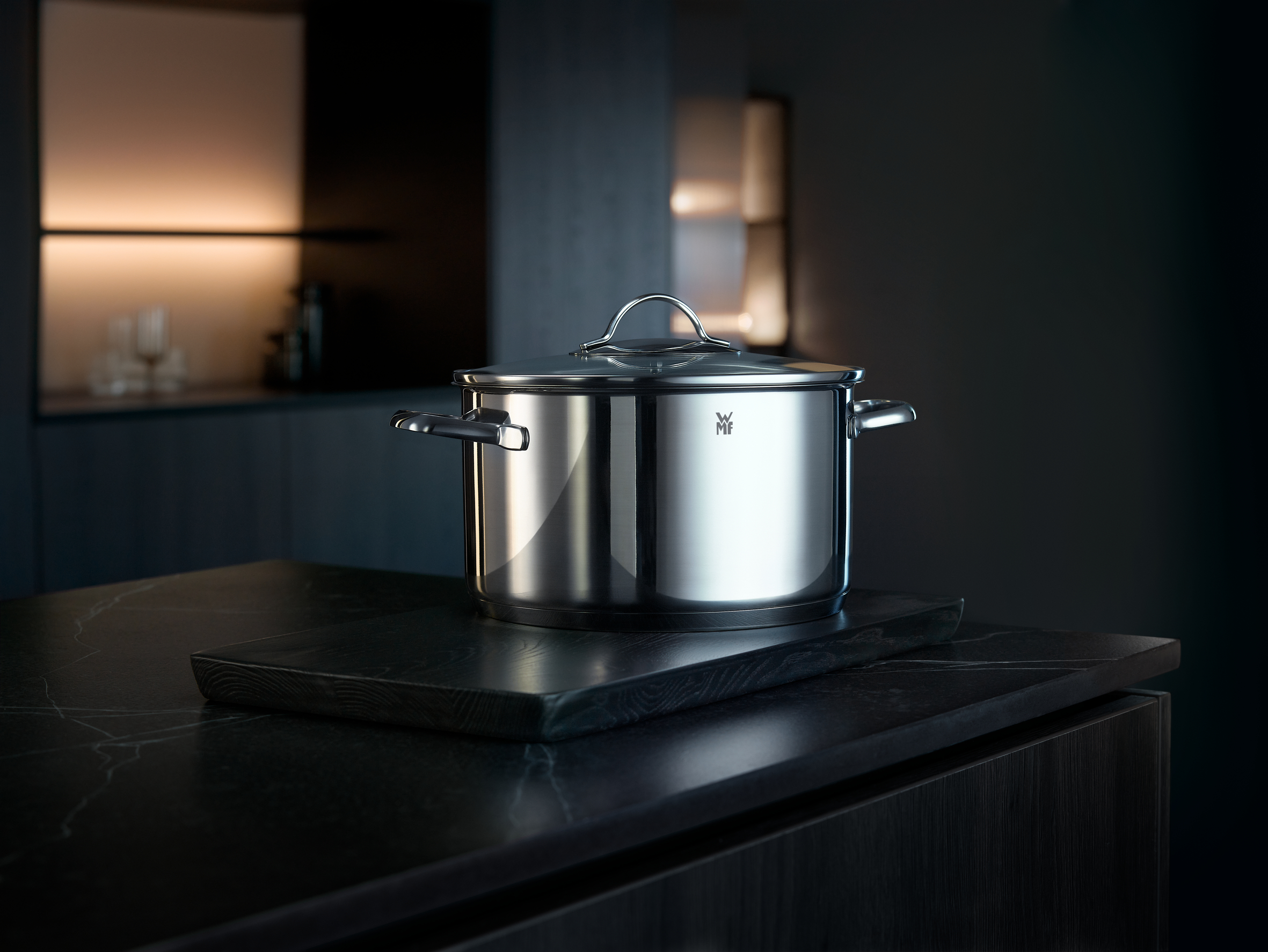 Une casserole en acier inoxydable sur une planche en bois, placée sur un comptoir sombre dans une cuisine.