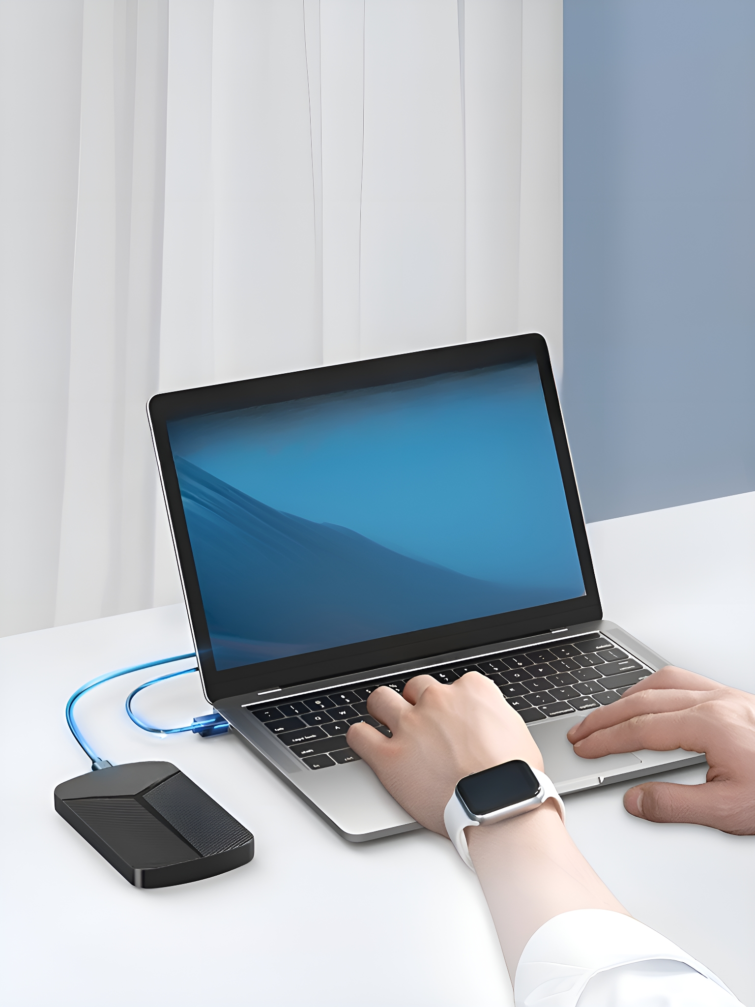 Laptop mit externer Festplatte verbunden. Eine Person tippt auf der Tastatur, trägt eine Smartwatch. Weißer Schreibtisch.