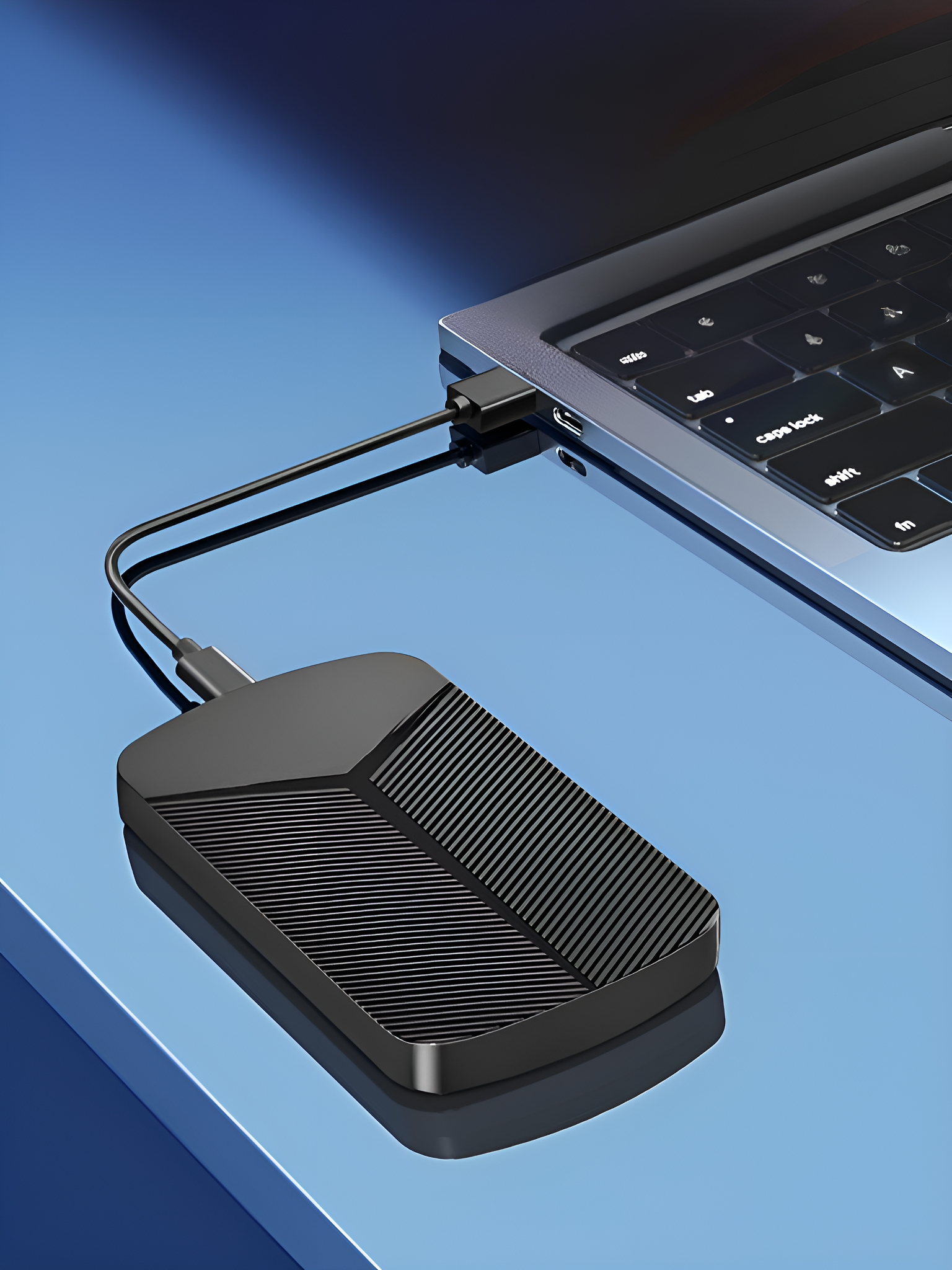 Eine schwarze externe Festplatte, die über ein USB-Kabel mit einem Laptop verbunden ist.