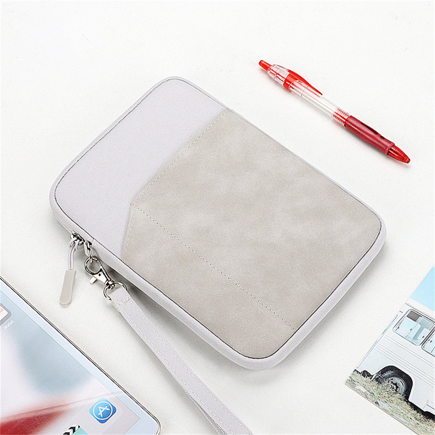 Eine hellgraue und weiße Tasche mit Reißverschluss, Riemen und Stift, mit einem Tablet sichtbar.