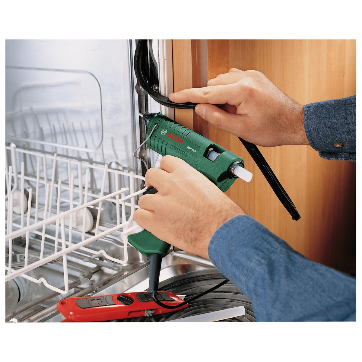 Osoba używa zielonego pistoletu do klejenia Bosch do uszczelniania czarnej gumowej uszczelki w zmywarce.