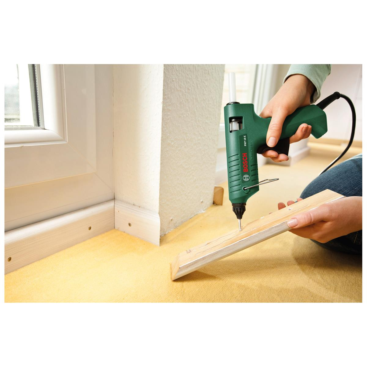 Osoba używa zielonego pistoletu do klejenia, aby przymocować kawałek drewna do powierzchni.