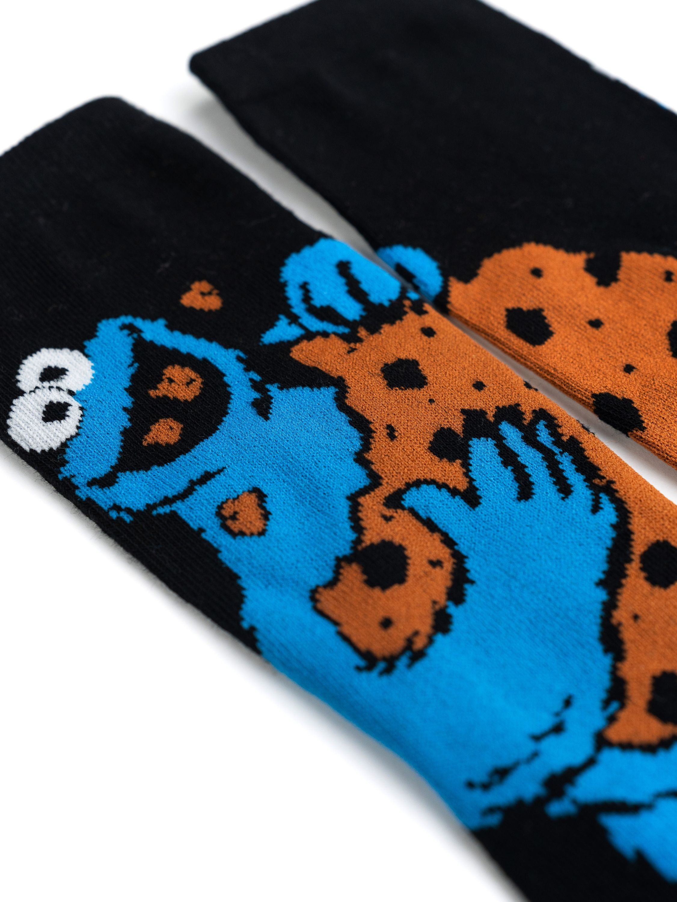 Blaue Cookie Monster Socken mit braunem Keks-Design auf schwarzen Socken, weißer Hintergrund.