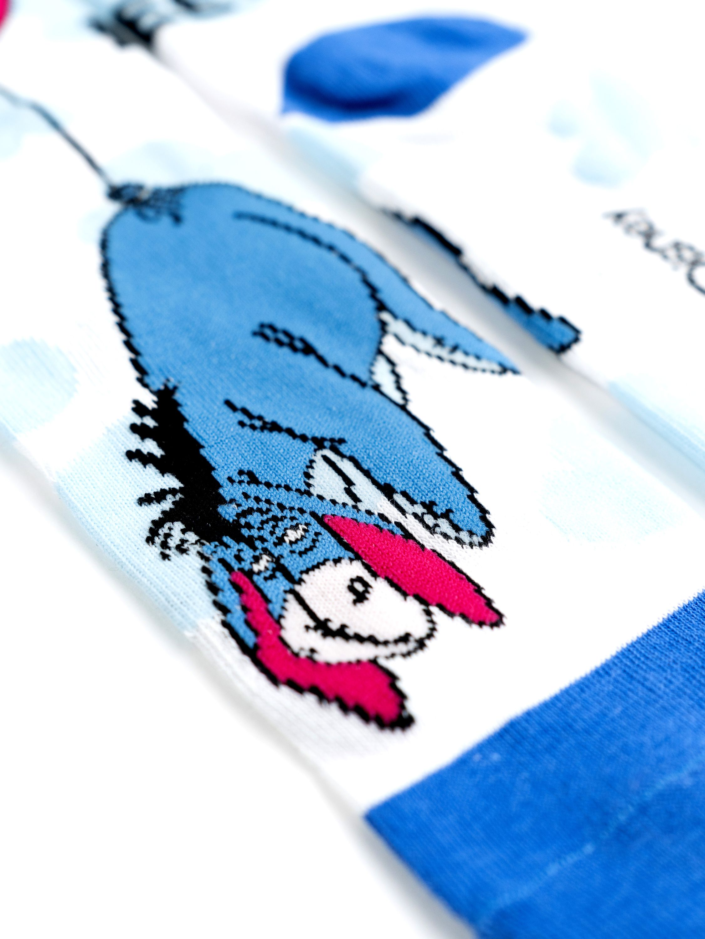Socken mit der Zeichentrickfigur Eeyore, in Blau und Weiß. Die Socken liegen auf weißem Untergrund.