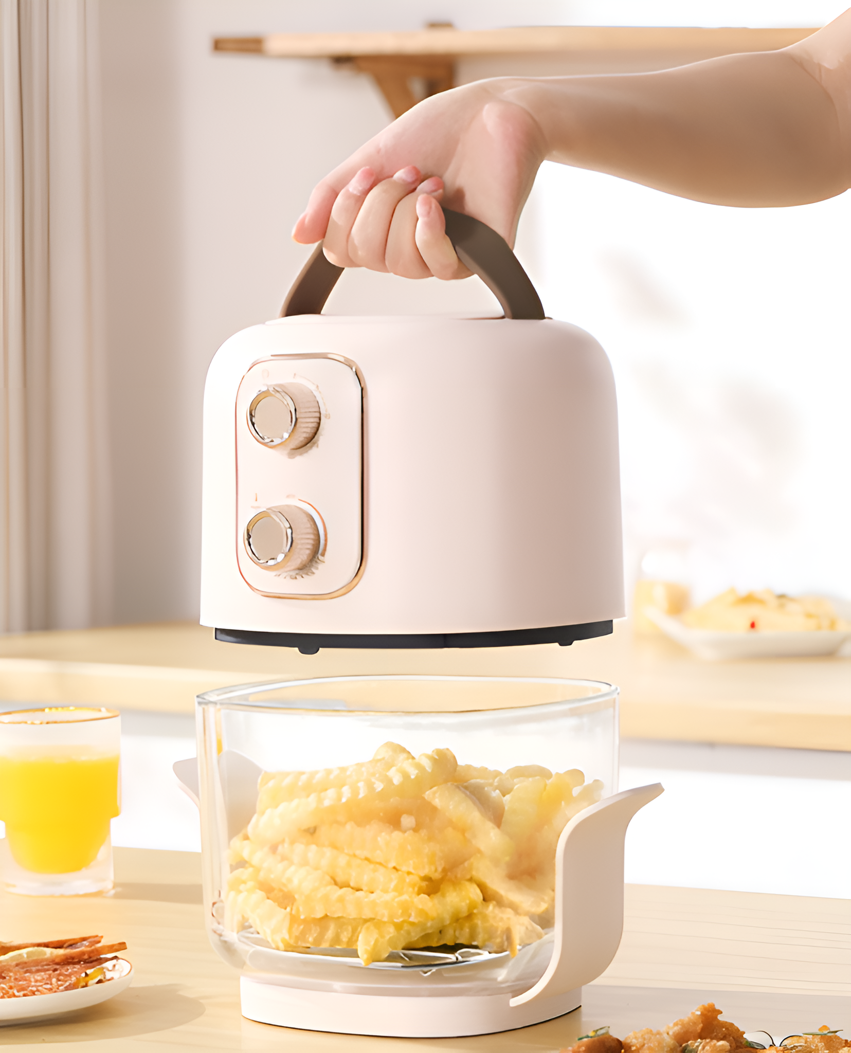 Die Hand einer Person hält eine kleine, hellrosa Fritteuse über einem durchsichtigen Behälter mit Pommes.