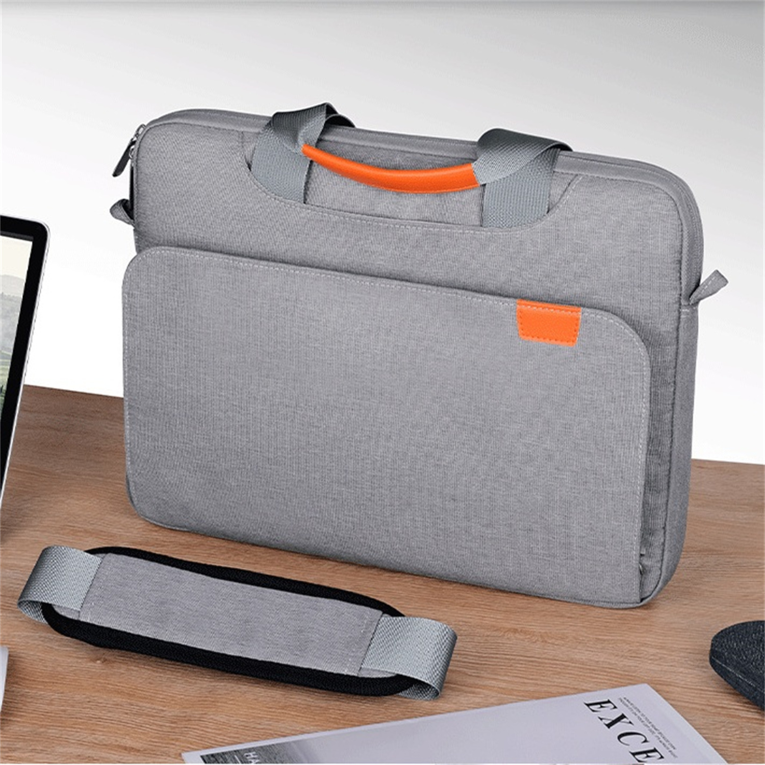 Graue Laptoptasche mit orangefarbenem Griff. Schultergurt und ein Buch.