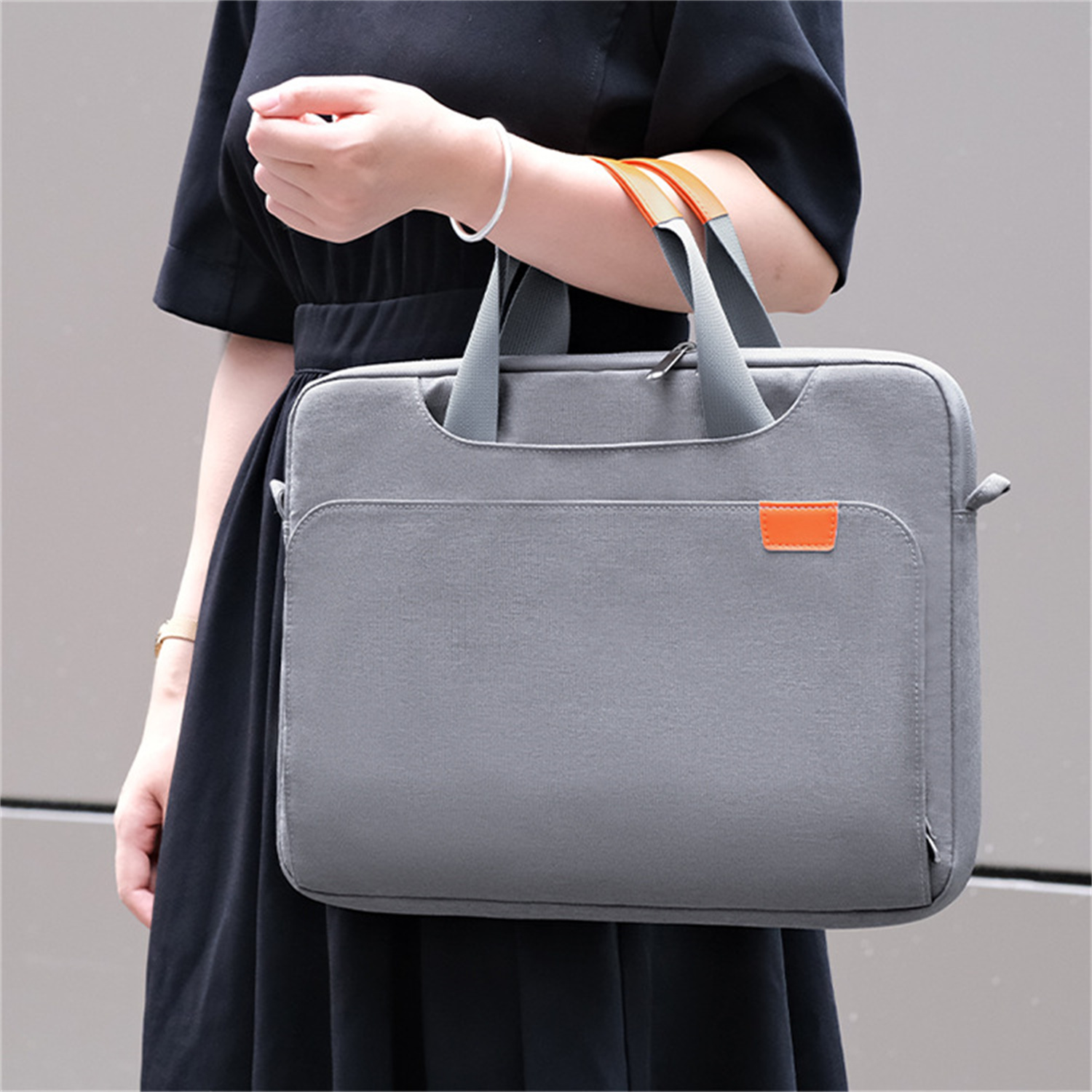 Eine Person in einem schwarzen Kleid hält eine graue Laptoptasche mit orangefarbenem Akzent.