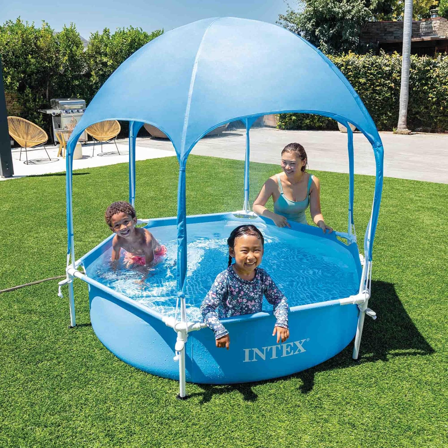 Tre bambini in una piscina blu sotto un tendone. Una donna in acqua.