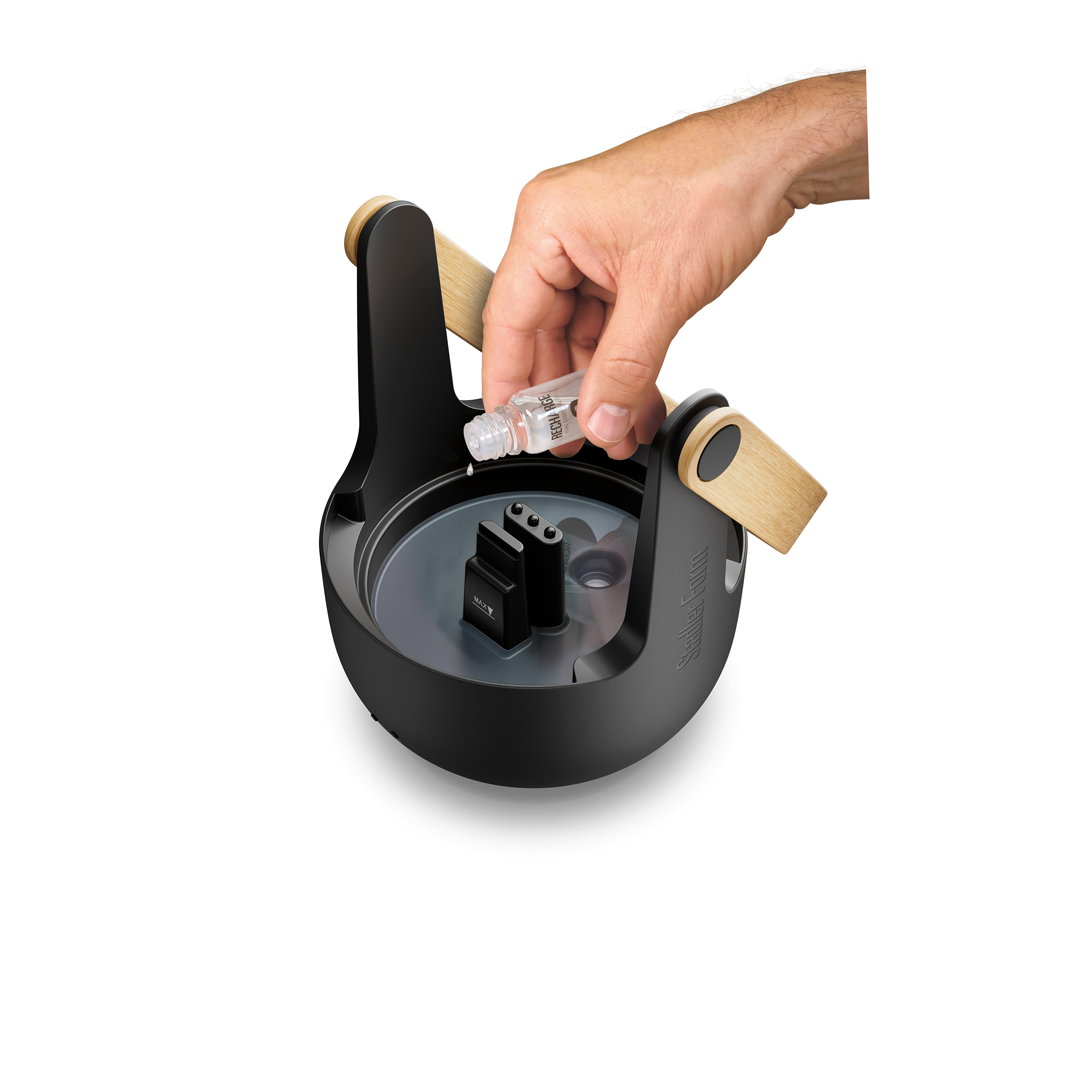 Ręka wlewa płyn z fiolki do czarnego urządzenia z drewnianymi uchwytami, na białym tle.