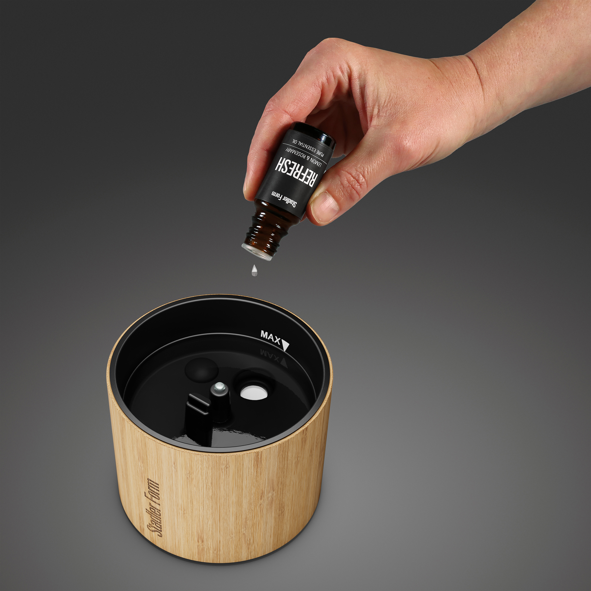 Hand pouring oil from a bottle into a diffuser. Gray background.