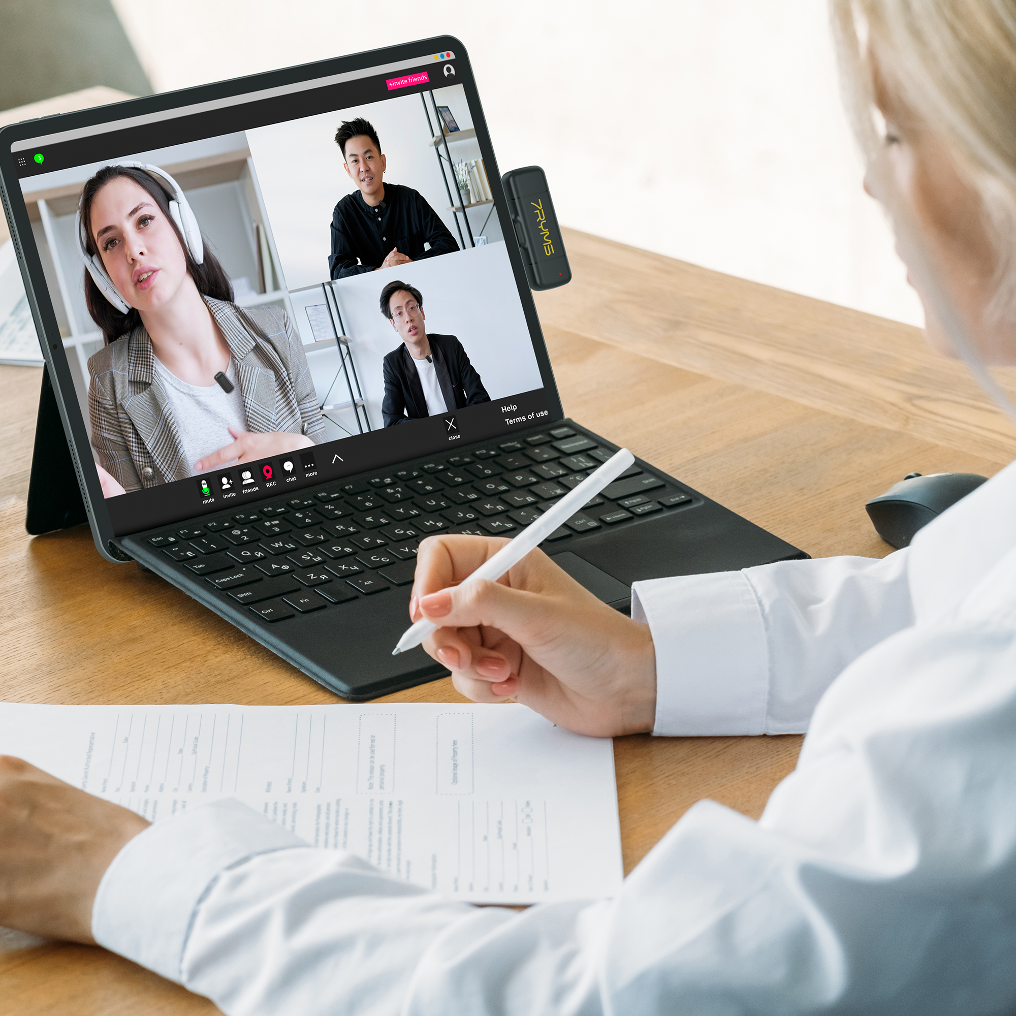 Eine Person führt einen Videoanruf auf einem Laptop und schreibt auf ein Dokument. Der Bildschirm zeigt 3 weitere Personen.