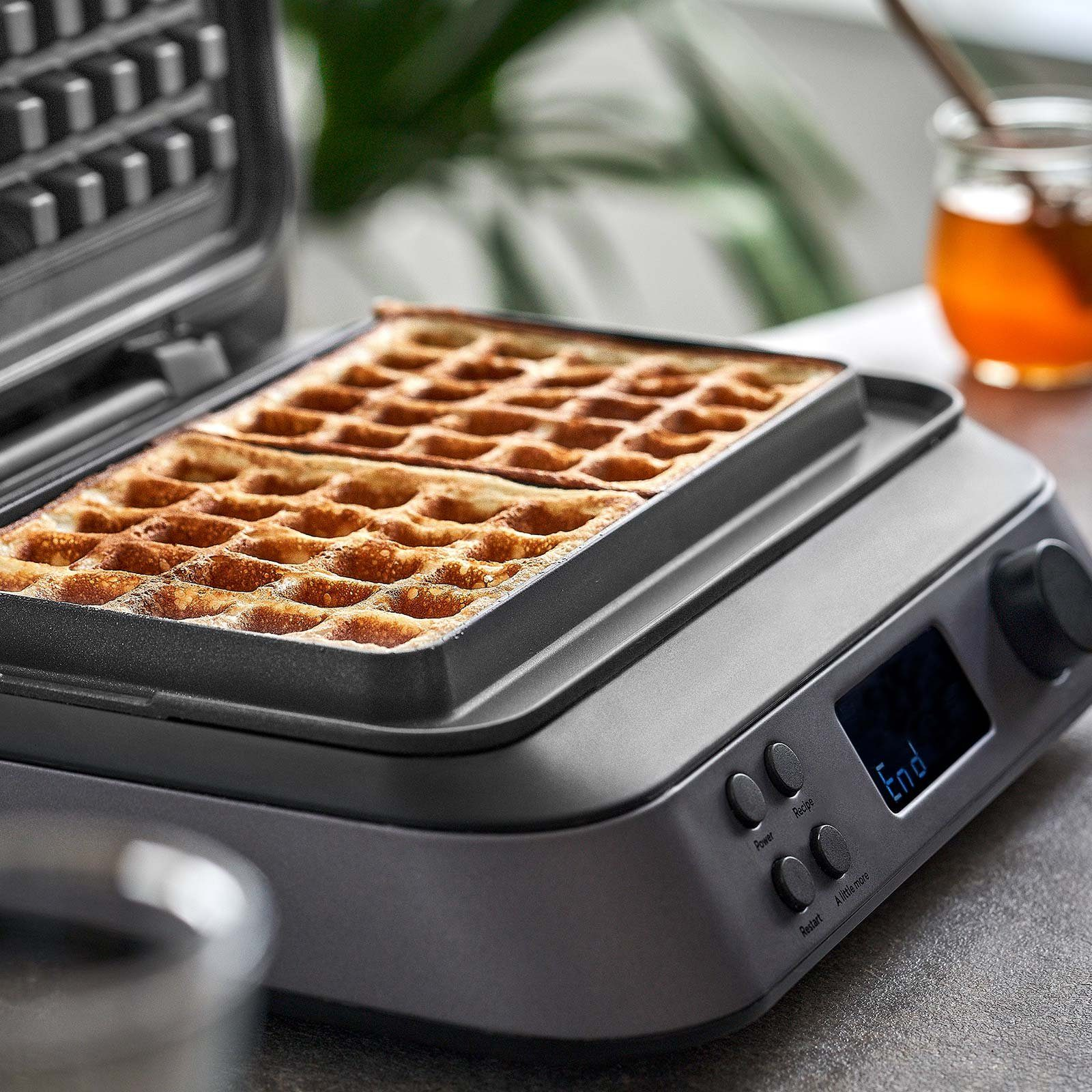 Ein Waffeleisen mit Waffeln darin und ein Glas Honig daneben.