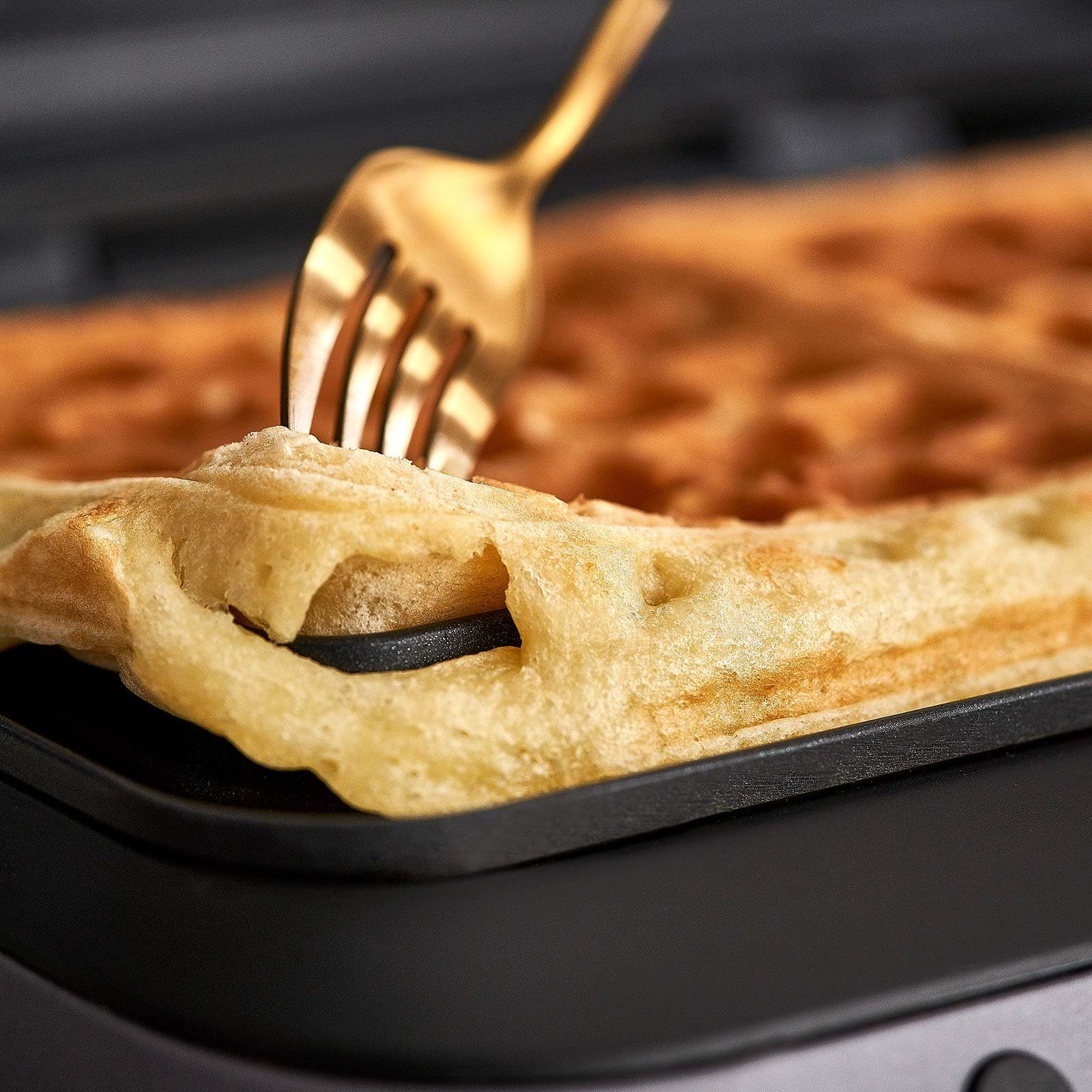 Nahaufnahme einer Waffel, die von einer goldenen Gabel angehoben wird. Goldbraune Farbe.