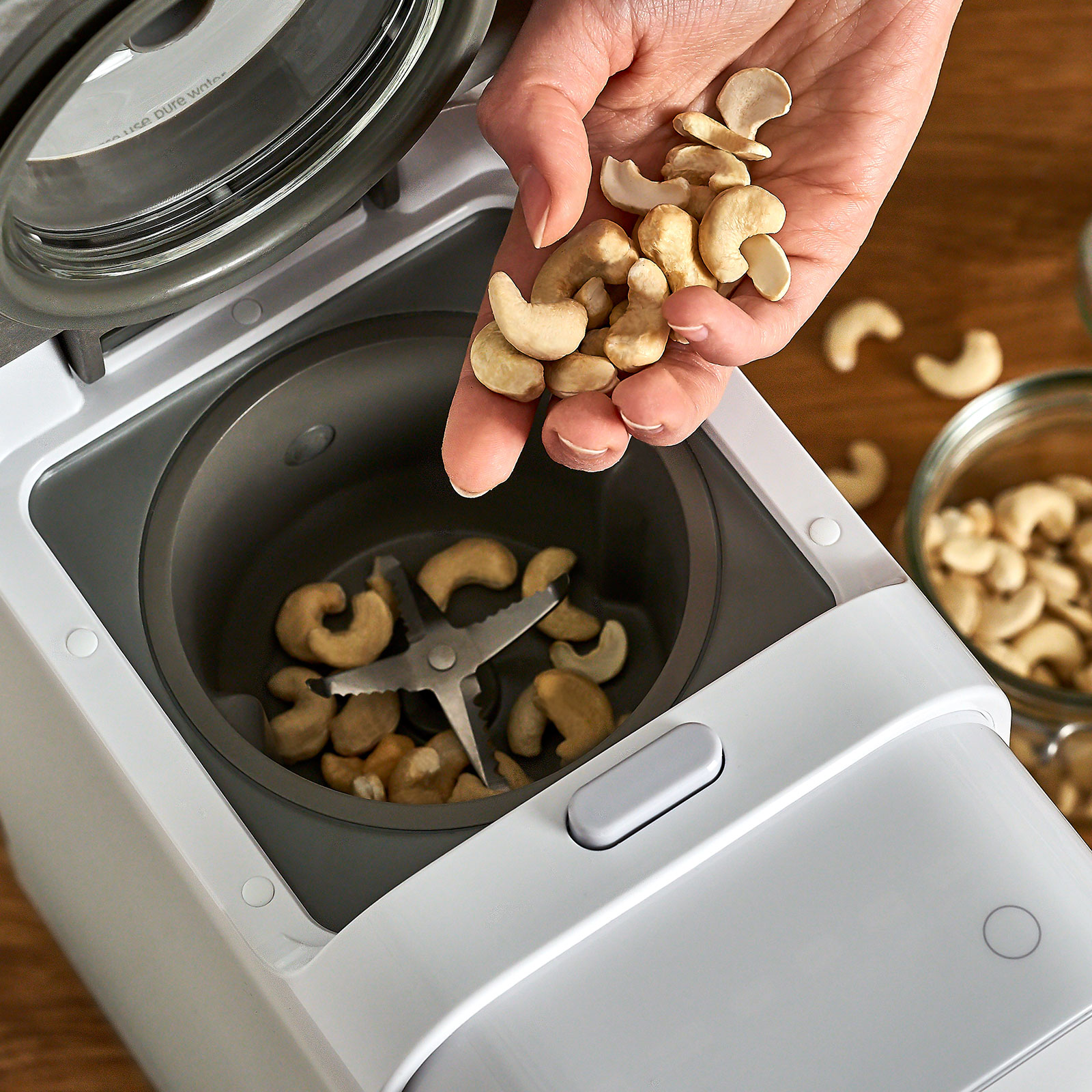 Hand gießt Cashewnüsse in einen Food Processor.