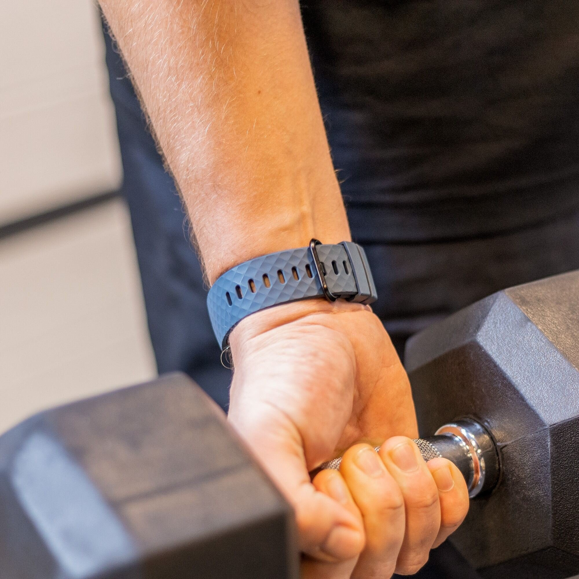 Handgelenk einer Person mit Fitnesstracker, hält eine Hantel. Arm und Hand sichtbar.