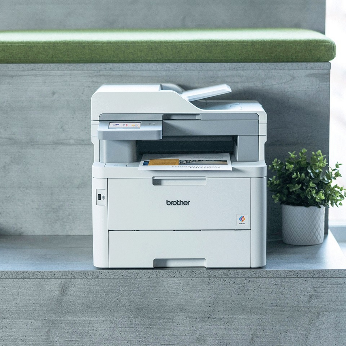 Witte printer op een bureau. Een groene bank op de achtergrond.