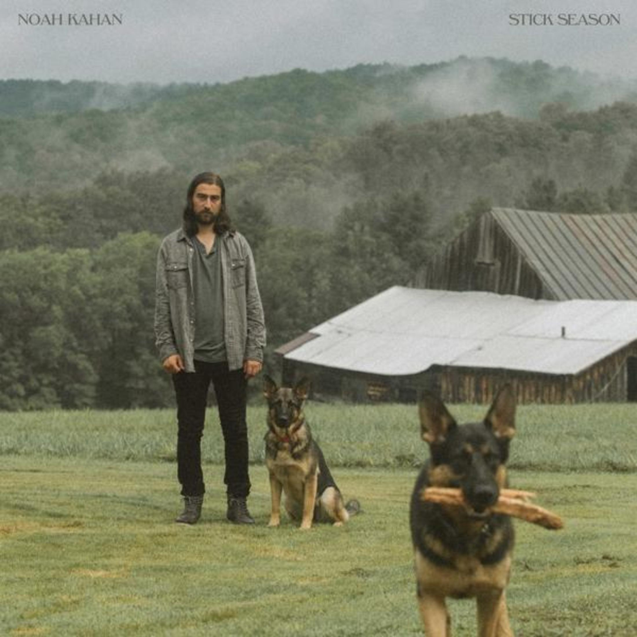 Copertina dell'album di Noah Kahan, Stick Season. Un uomo è in piedi con due cani in un campo, un fienile sullo sfondo.