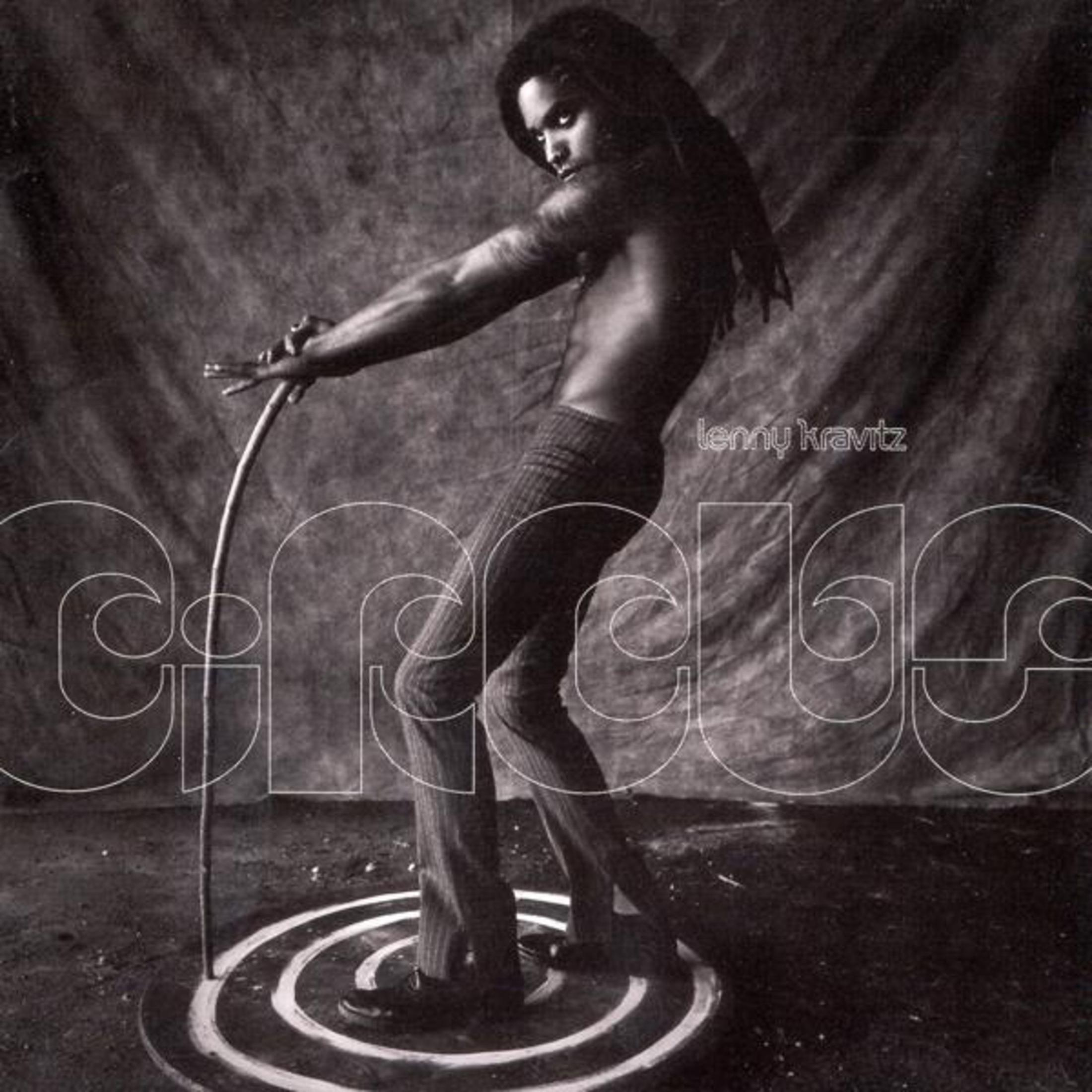 Lenny Kravitz, image en noir et blanc, debout sur un cercle et tenant un bâton en métal. Couverture.