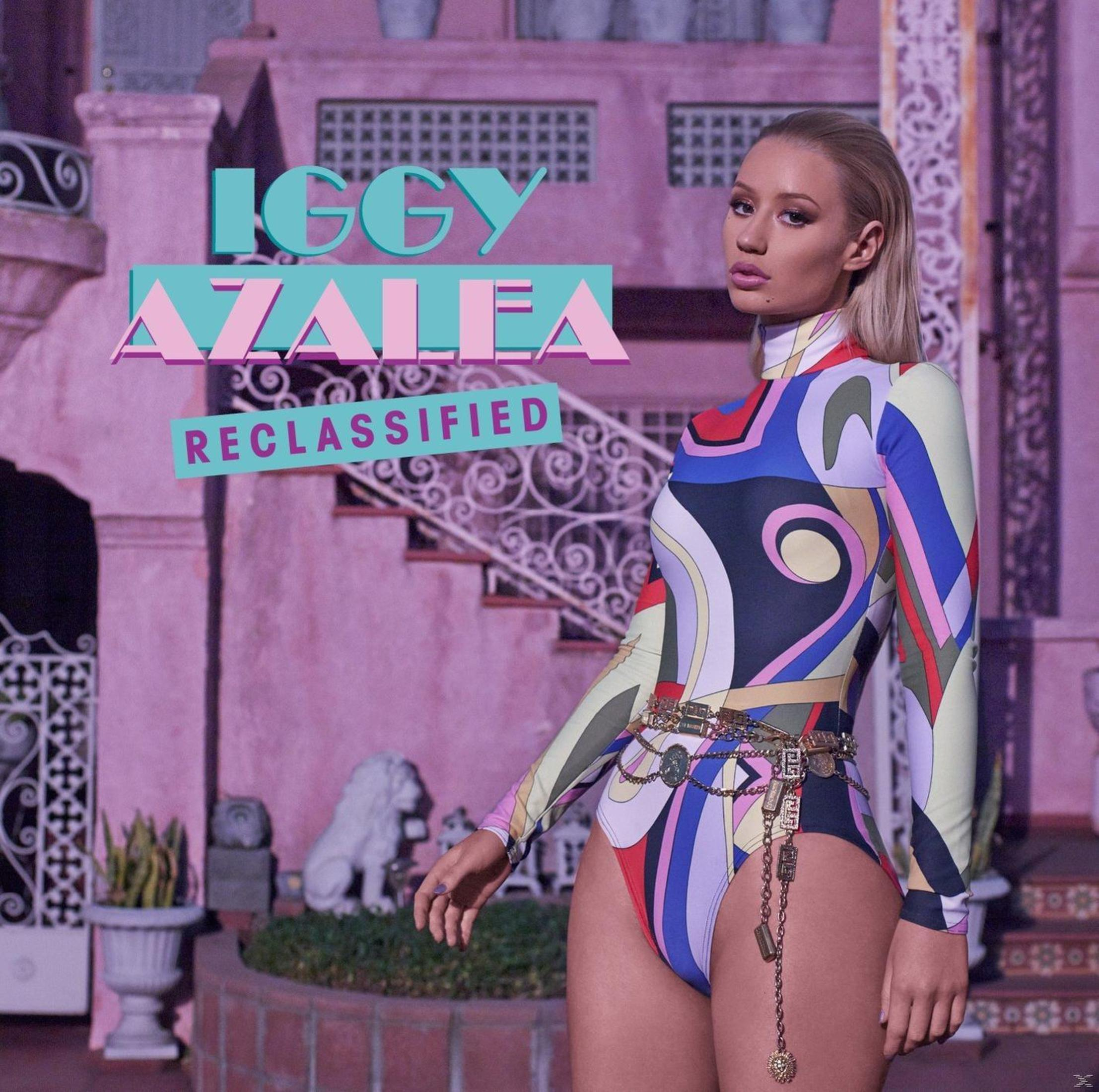 Albumhoes met Iggy Azalea in een kleurrijk turnpakje die buiten een gebouw staat.