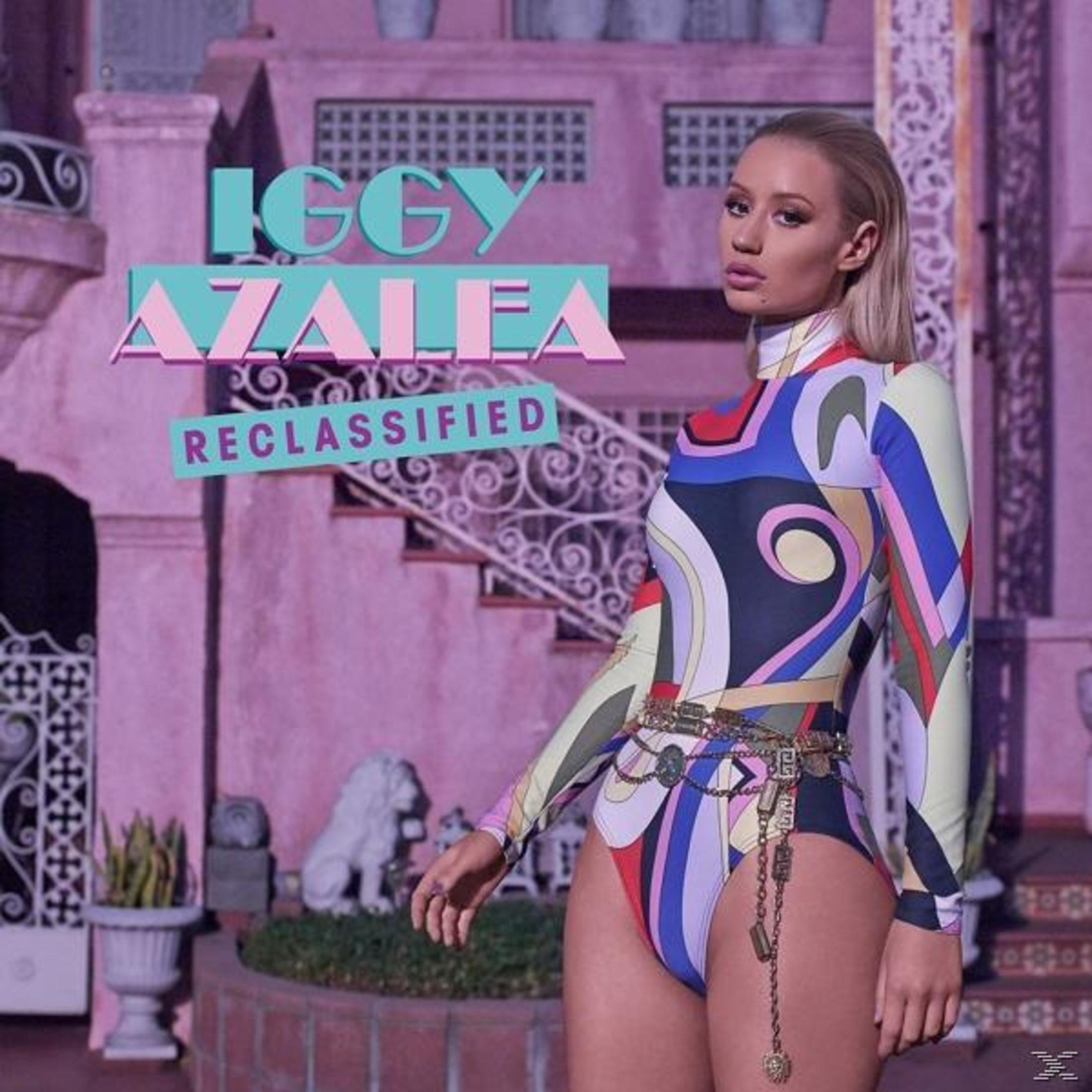 Albumhoes van Iggy Azalea. De artiest draagt een kleurrijke outfit voor een roze gebouw.