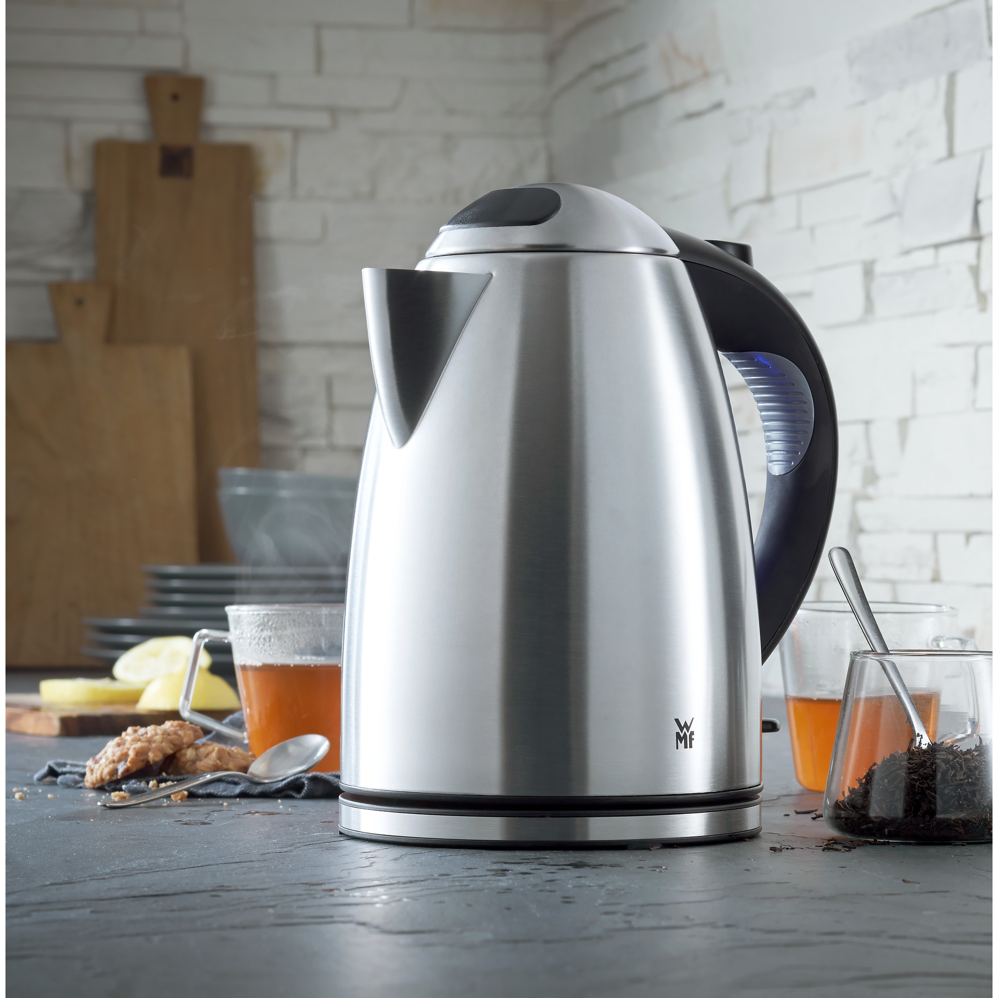 Hervidor eléctrico de acero inoxidable con tazas de té y galletas.