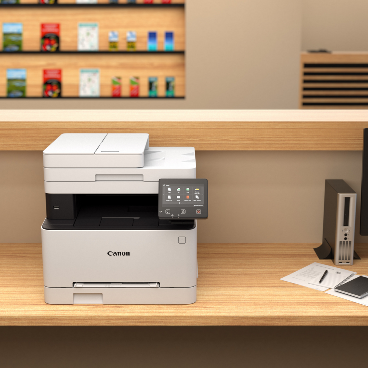 Biała drukarka Canon na drewnianym biurku z ekranem, obok komputera.