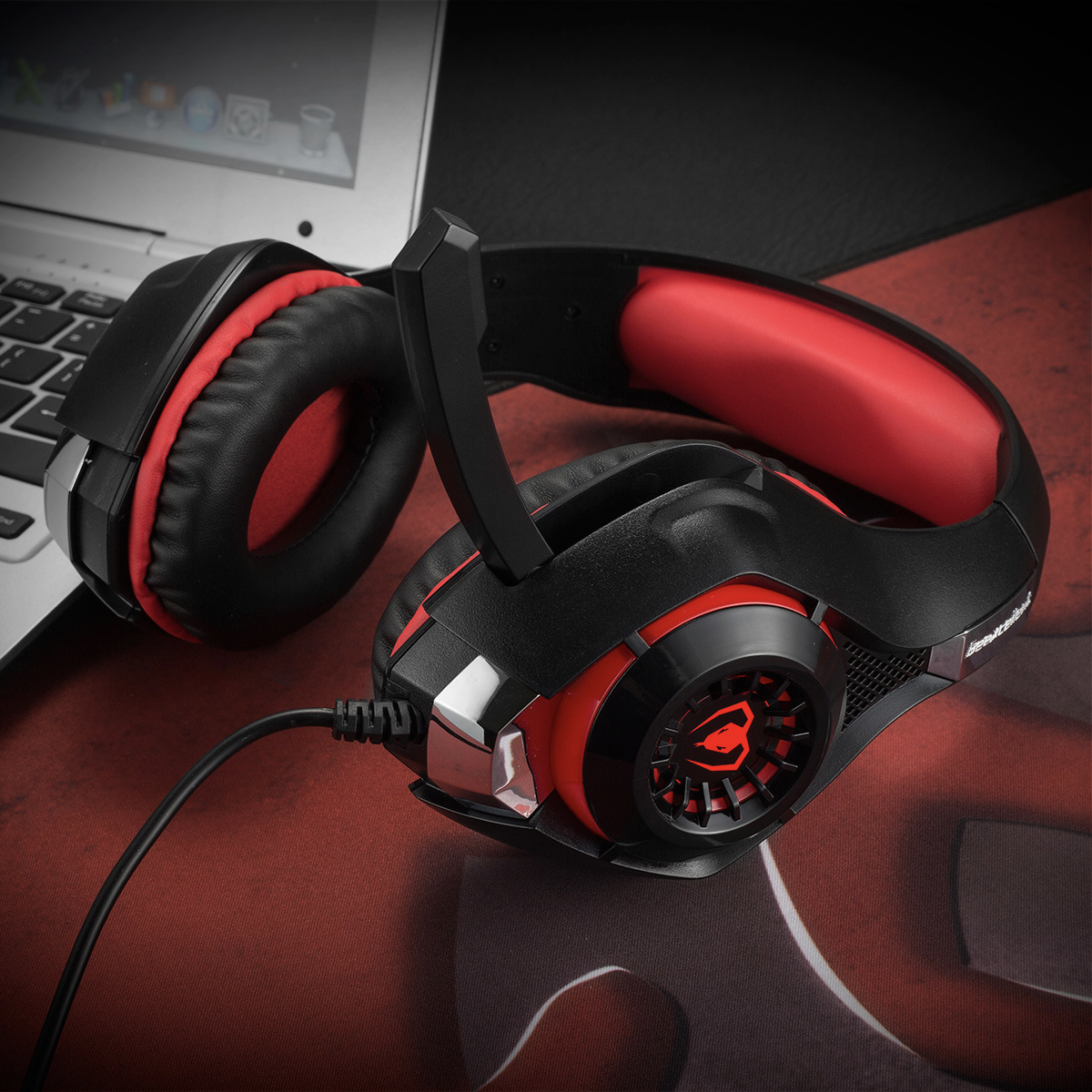 Gaming-Headset: schwarzes und rotes Design, mit der linken Ohrmuschel über einem Laptop.
