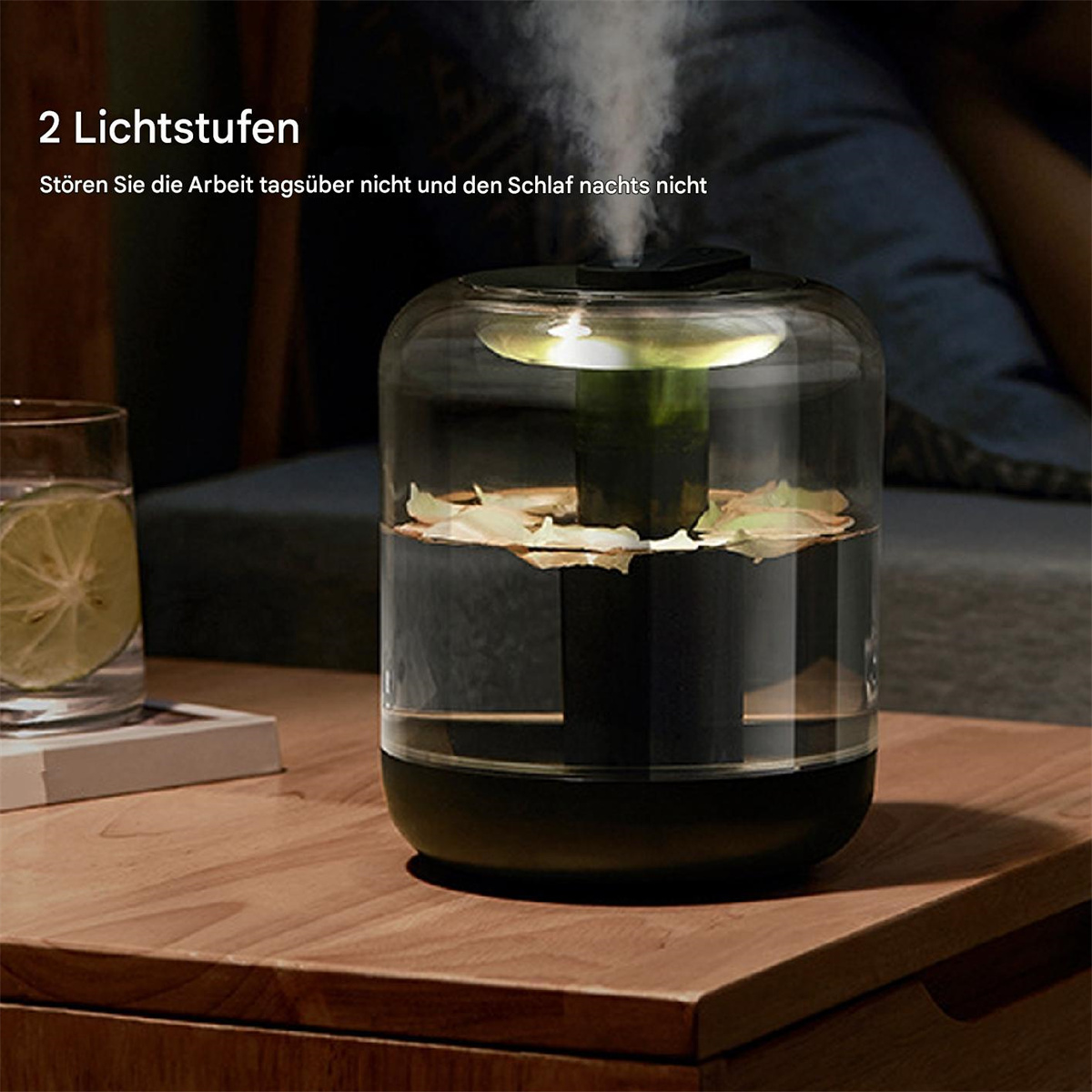 Ein Glas-Luftbefeuchter mit Wasser und Blättern auf einem Holztisch. Dampf kommt von oben.
