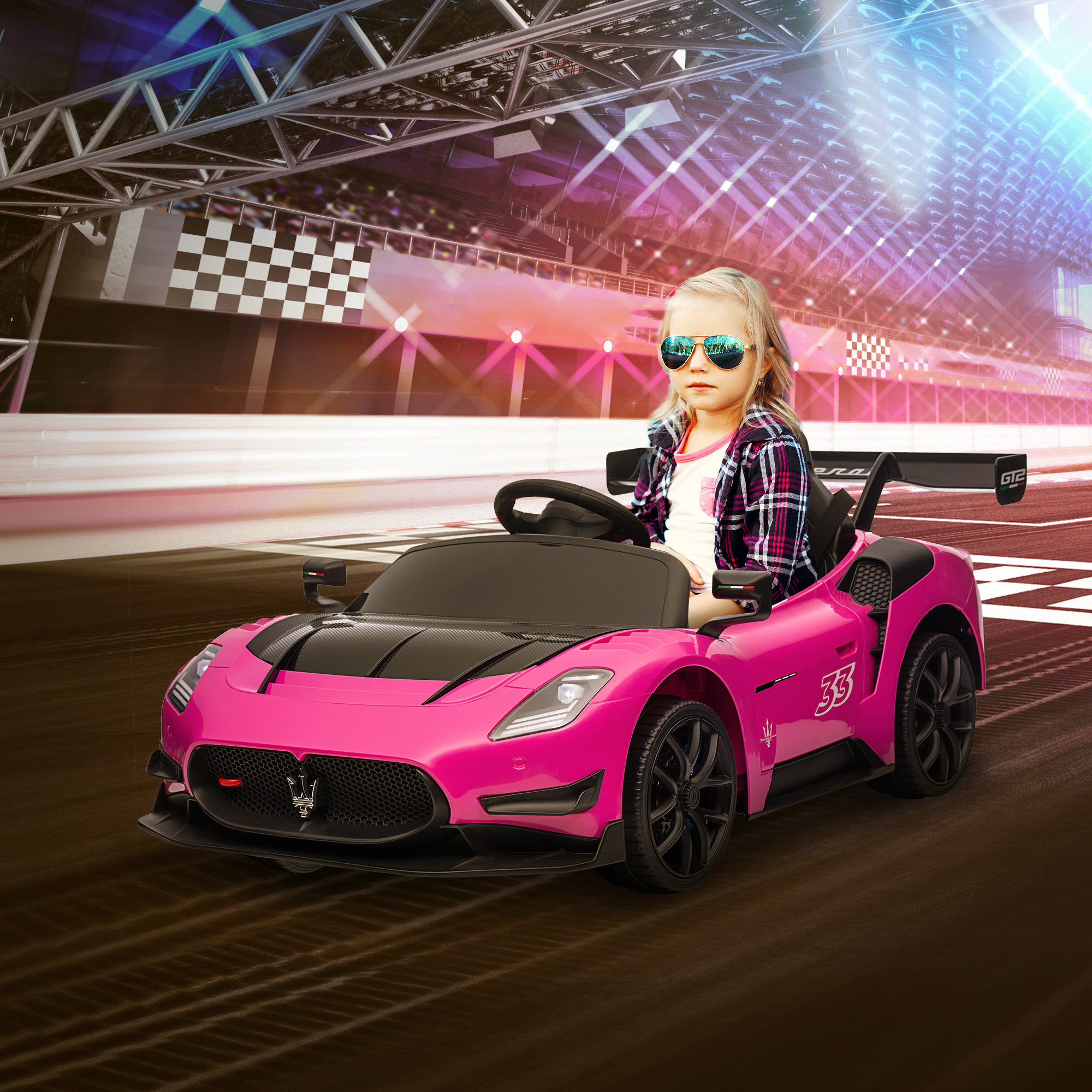 Una niña con gafas de sol está sentada en un coche Maserati rosa para niños en una pista de carreras.