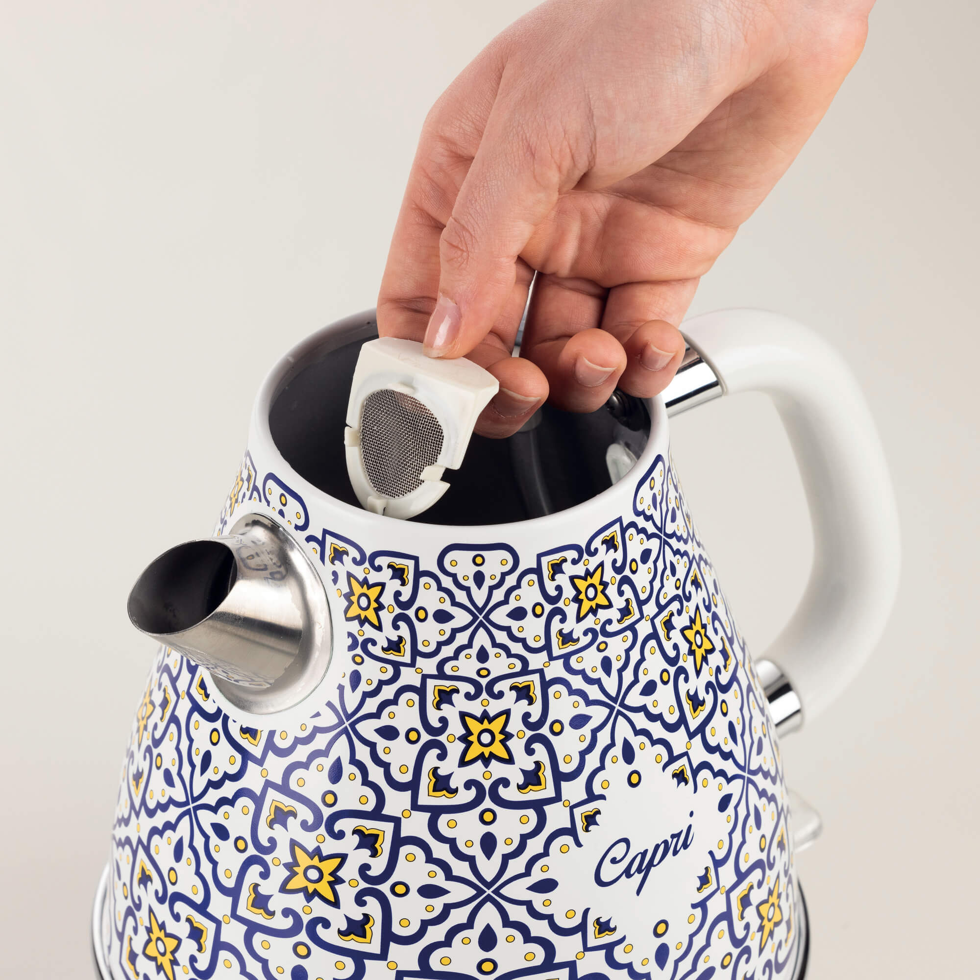 Ręka wkłada filtr do wzorzystego, biało-niebieskiego czajnika elektrycznego z czarnym dziobkiem.