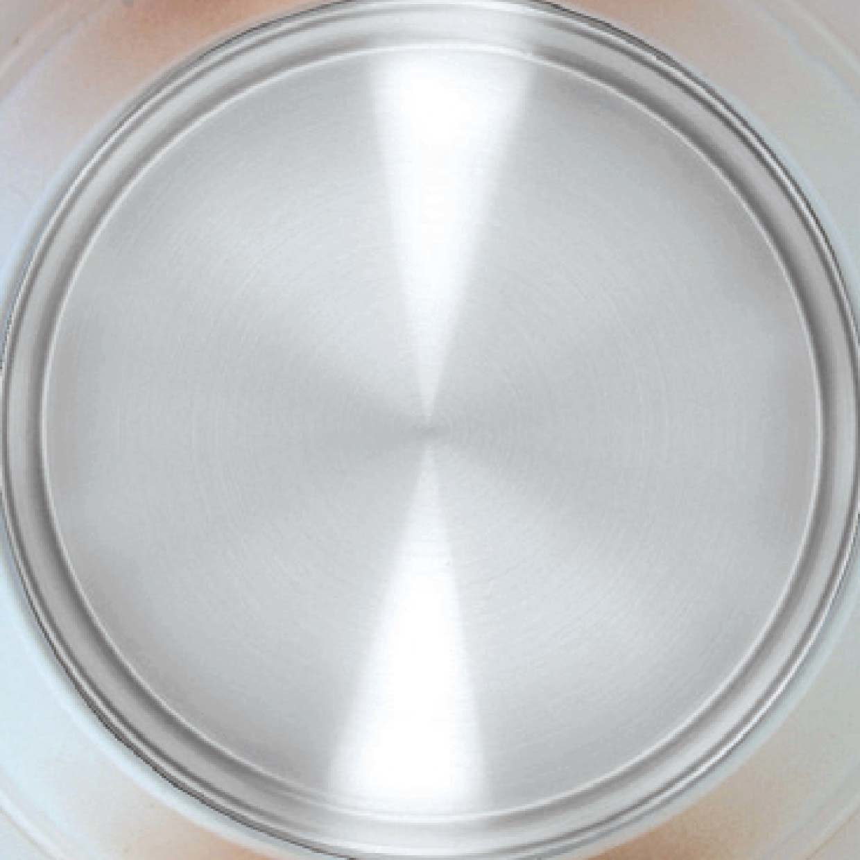 Nahaufnahme einer glänzenden, silbernen Metallplatte. Die Platte ist kreisförmig und die Oberfläche reflektiert Licht.