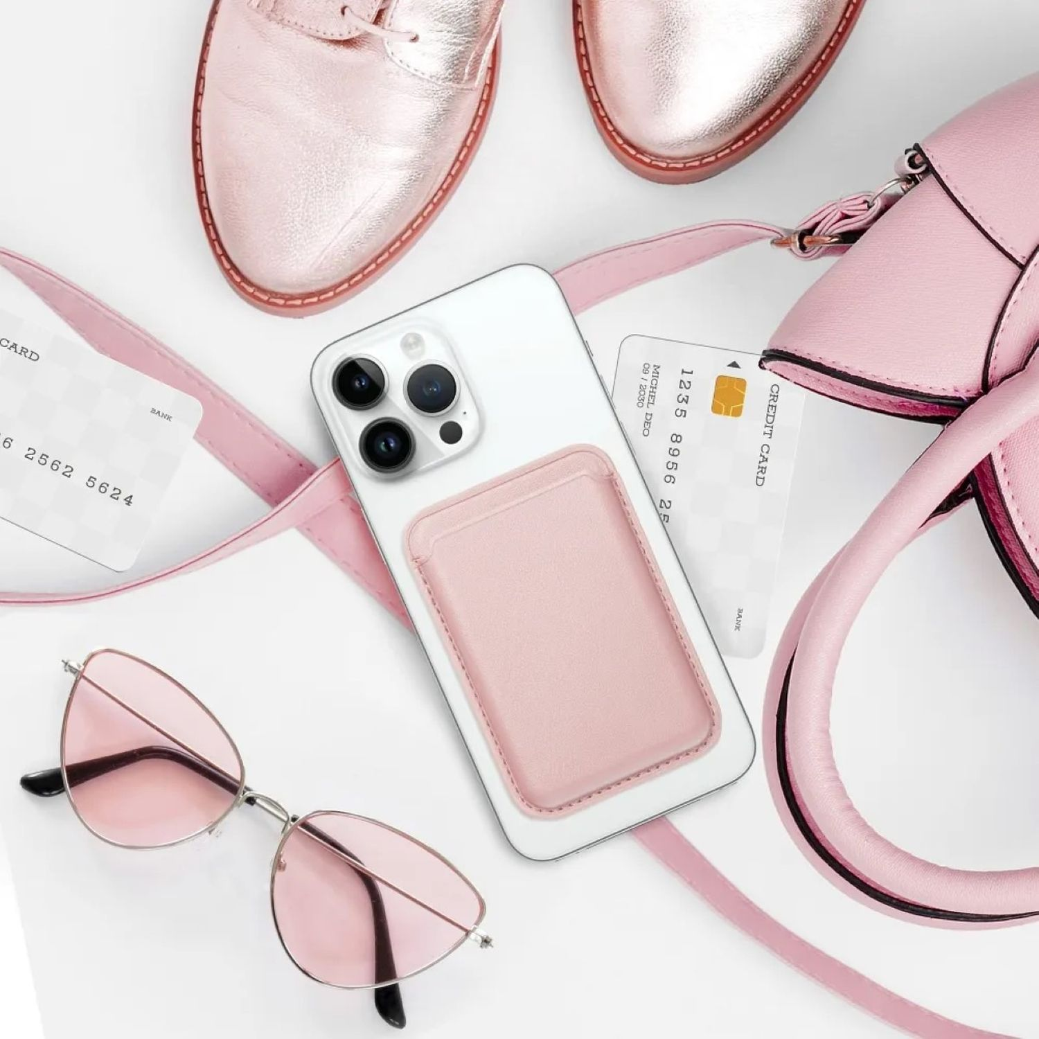 Ein Telefon mit rosa Kartenhalter, Sonnenbrille und Handtasche auf weißer Oberfläche.