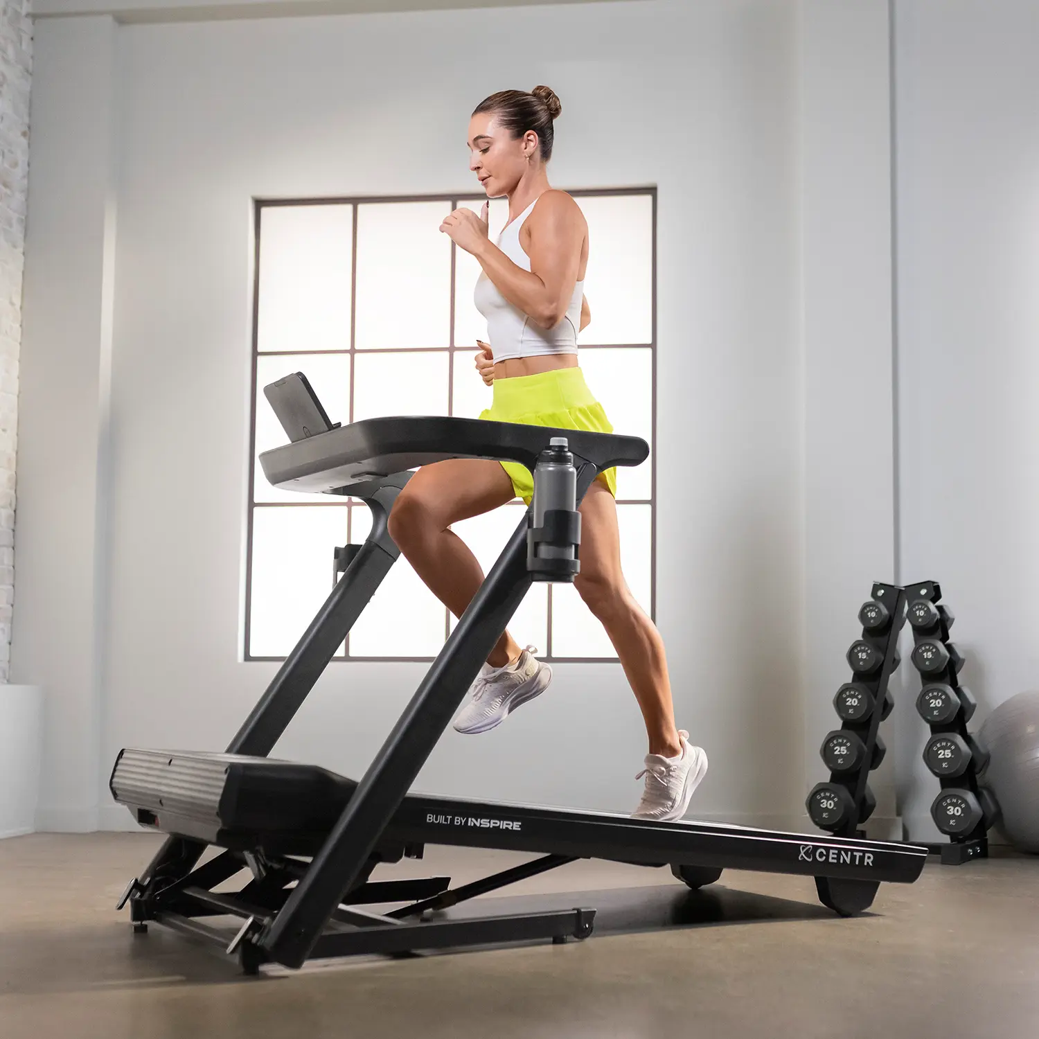 Woman running on a treadmill. White top, yellow shorts. Gym equipment in the background.