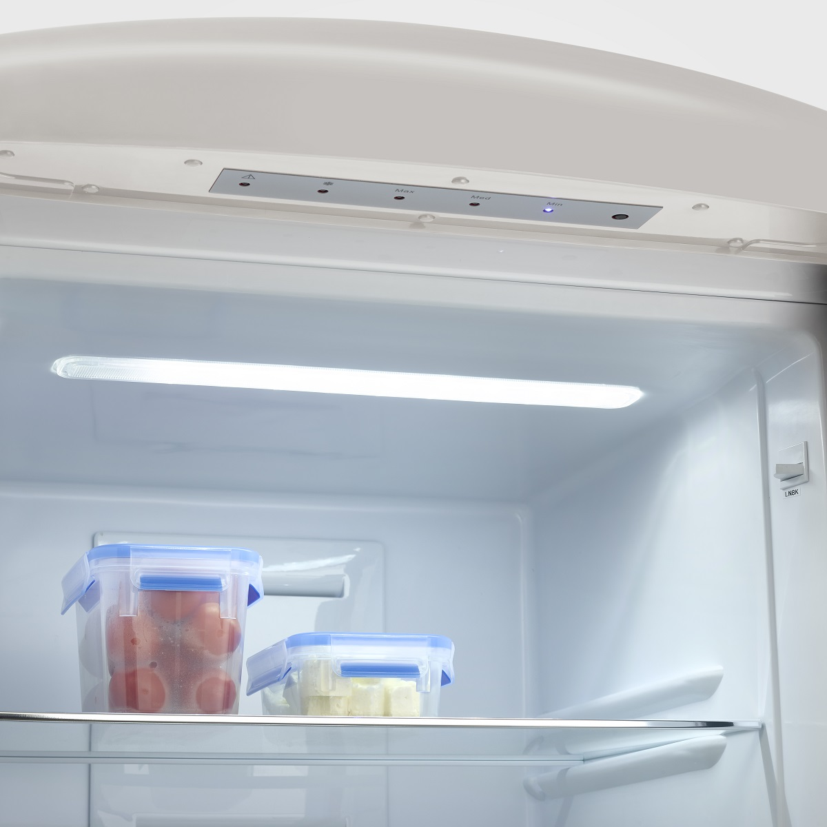 All'interno di un frigorifero: pomodori e formaggio in contenitori su uno scaffale e una luce.