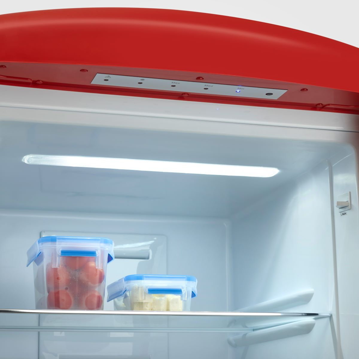 Wewnątrz lodówki z plastikowymi pojemnikami wypełnionymi pomidorami i serem.