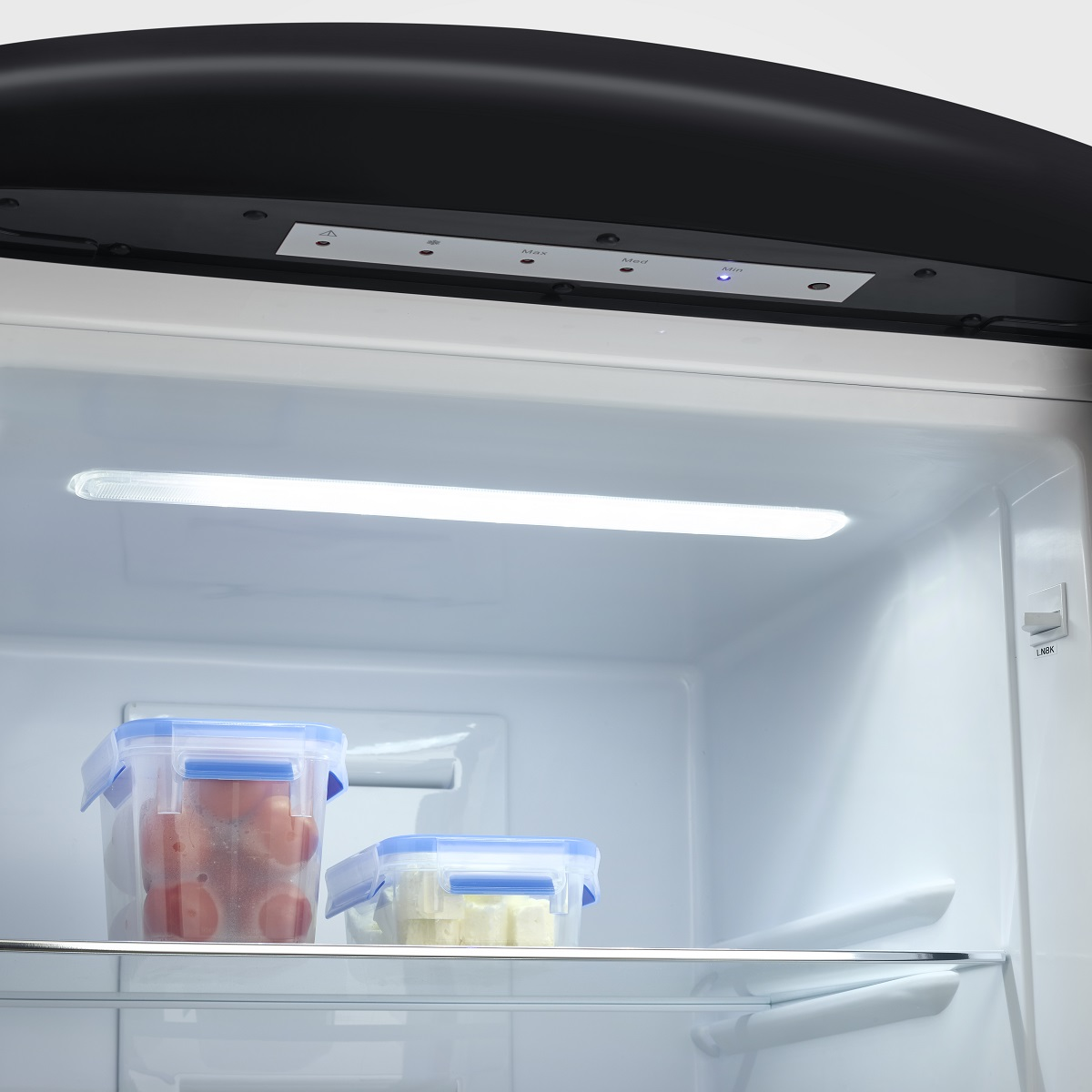 Inside a refrigerator with two food containers. One has red tomatoes, the other white cheese.