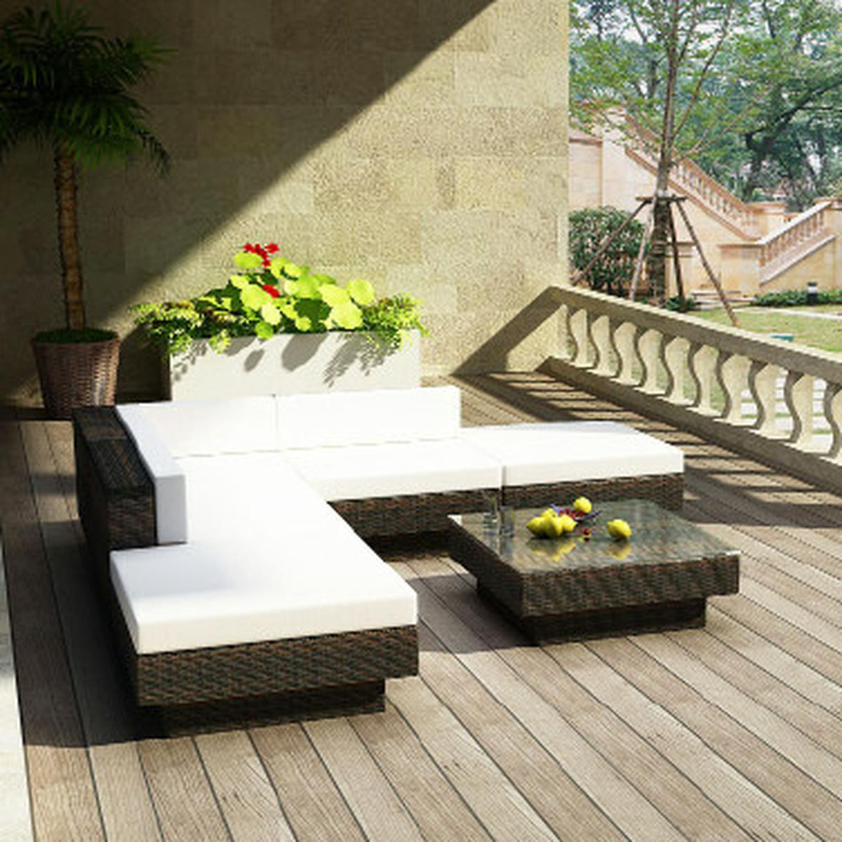 Outdoor-Sitzbereich mit weißen Kissen, braunen Korbmöbeln und Holzterrasse.