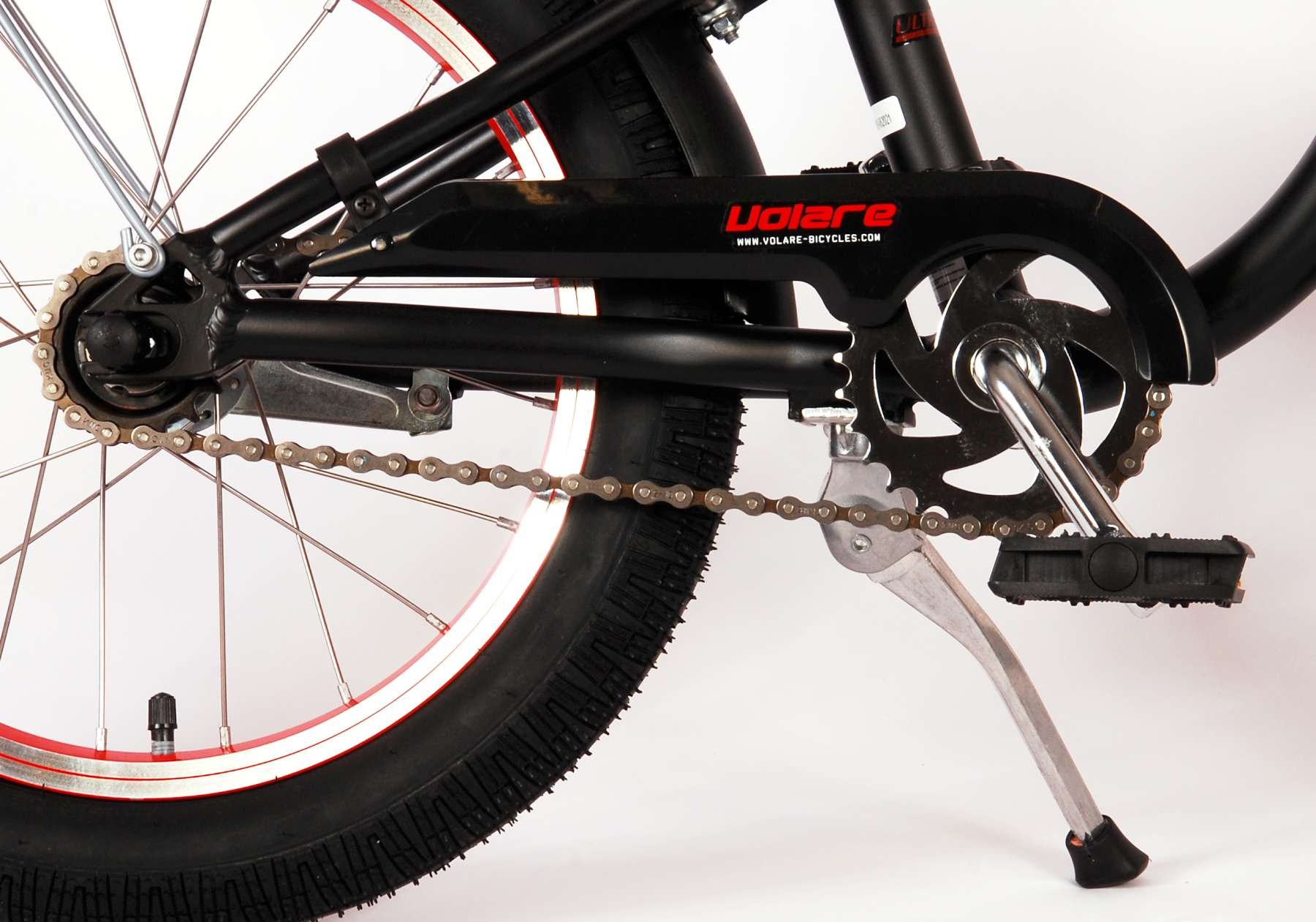 Nahaufnahme von schwarzer Fahrradkette, Pedalen und Volare-Logo auf schwarzem Rahmen.