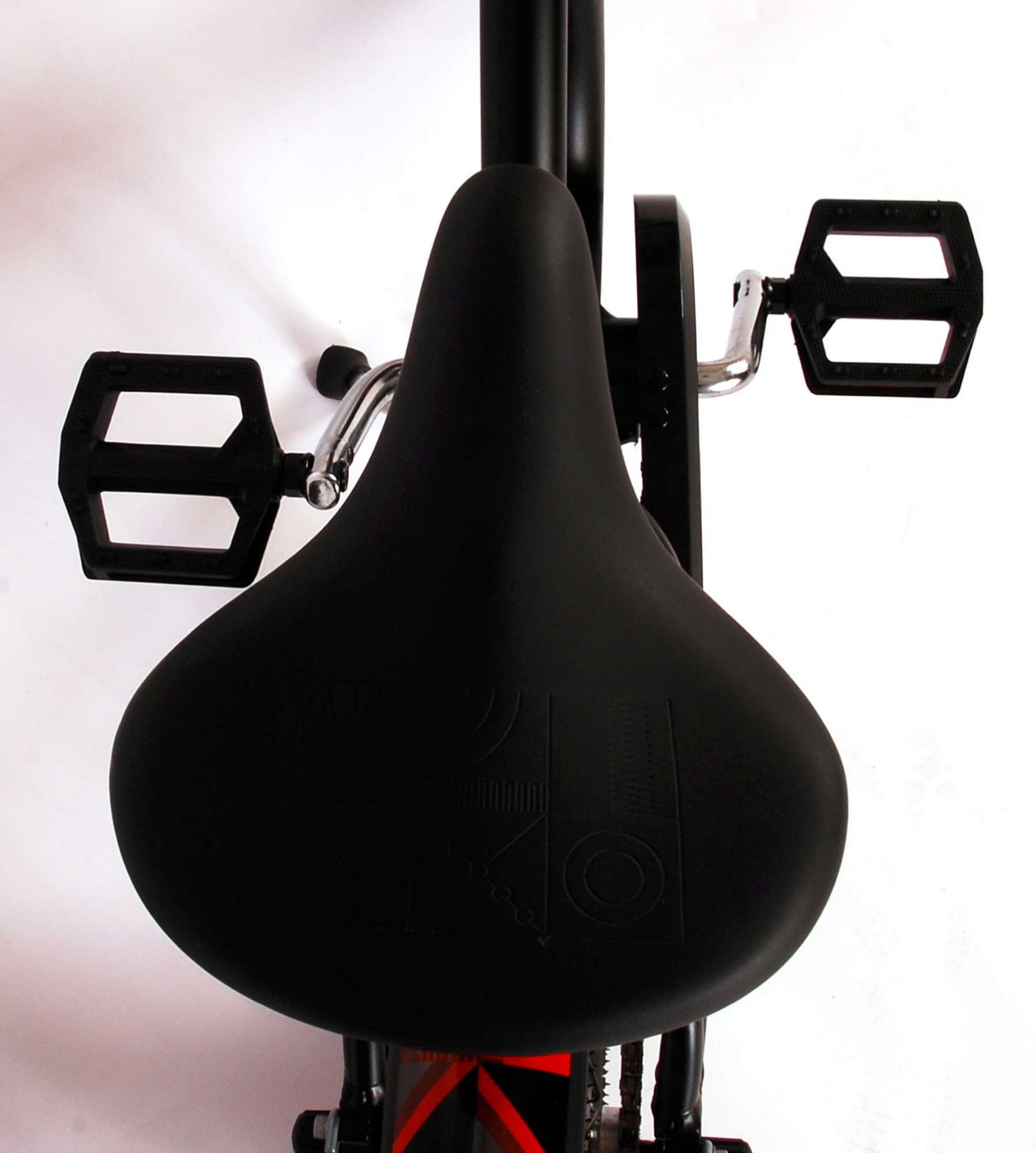 Schwarzer Fahrradsattel, schwarze Pedale und rote Linie. Weißer Hintergrund. Sattel sagt 'Volare'.