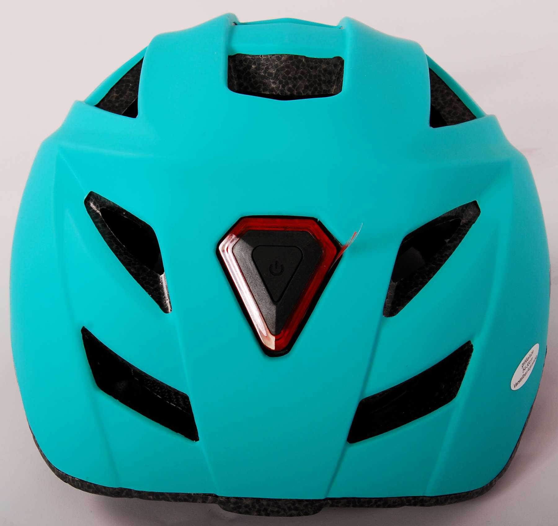 Ein türkisfarbener Fahrradhelm mit rotem Licht und einem Ein- und Ausschalter auf der Rückseite. Der Hintergrund ist eine weiße Oberfläche.