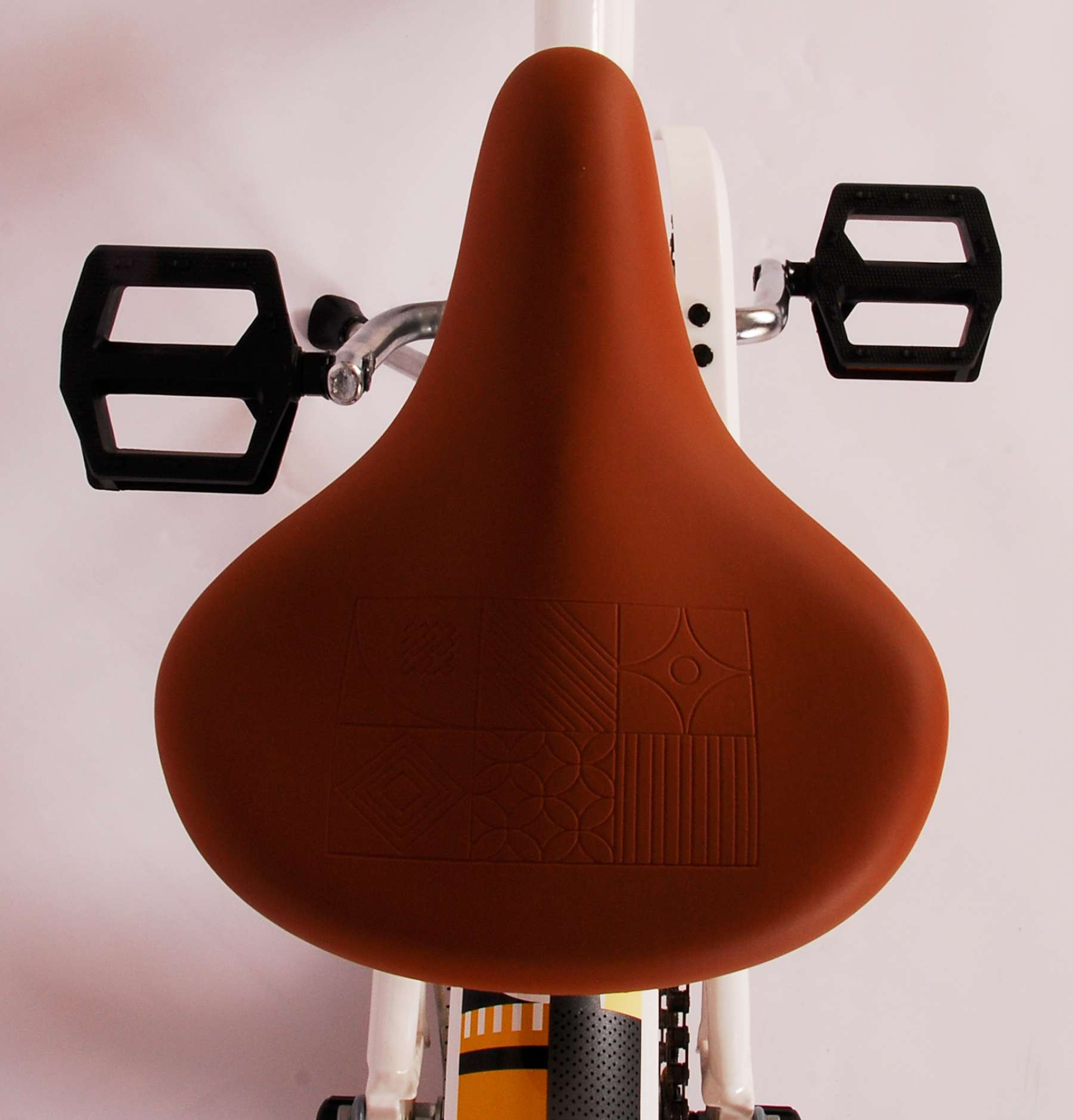 Nahaufnahme eines braunen Fahrradsattels mit gemustertem Design und schwarzen Pedalen.