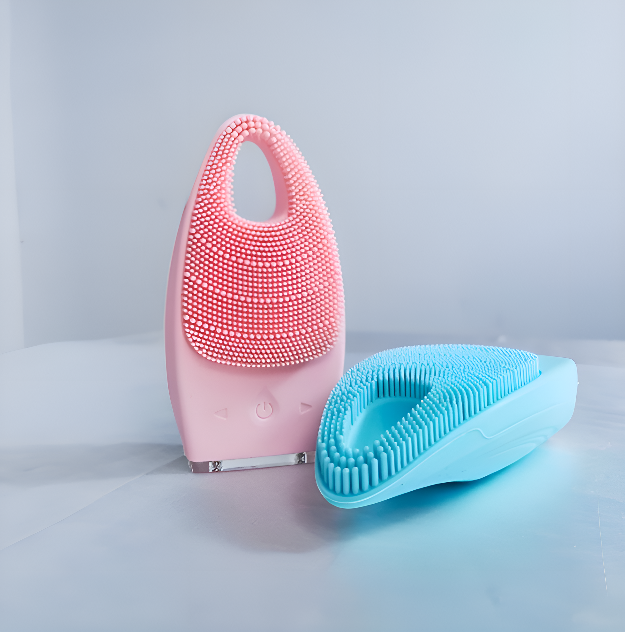 Zwei Gesichtsreinigungsgeräte. Eines rosa, eines blau. Beide haben Silikonborsten. Das rosa steht aufrecht.