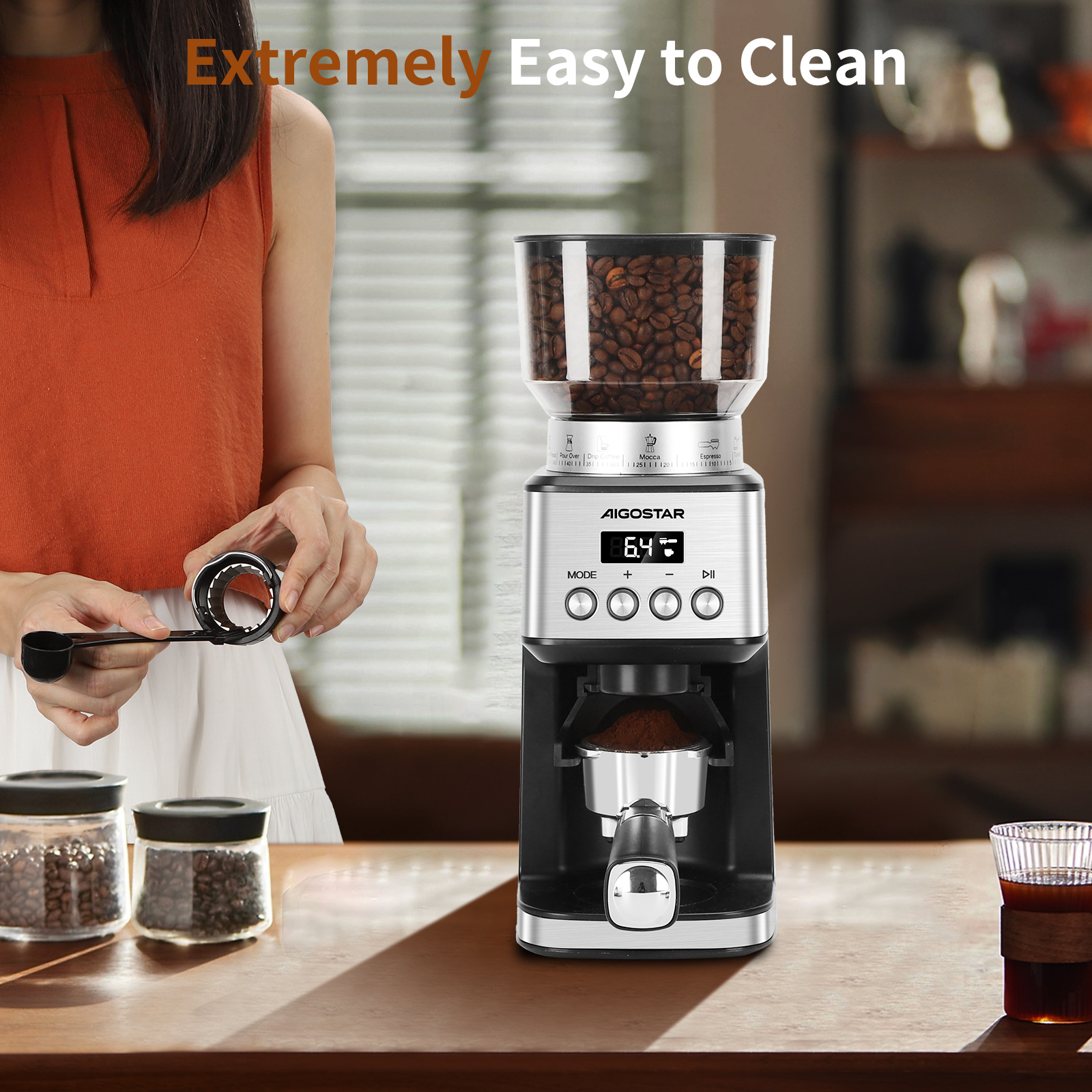 Un molinillo de café plateado y negro con granos de café en un recipiente y café molido en un filtro.