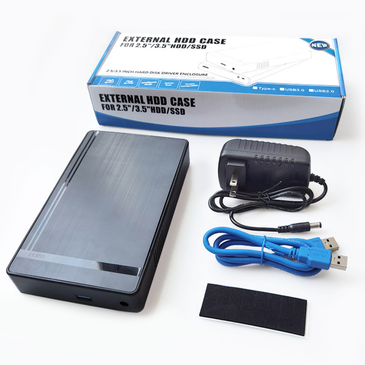 Externe HDD-Hülle mit Box, Netzteil, USB-Kabel und einem schwarzen Klebepad auf weißem Hintergrund.