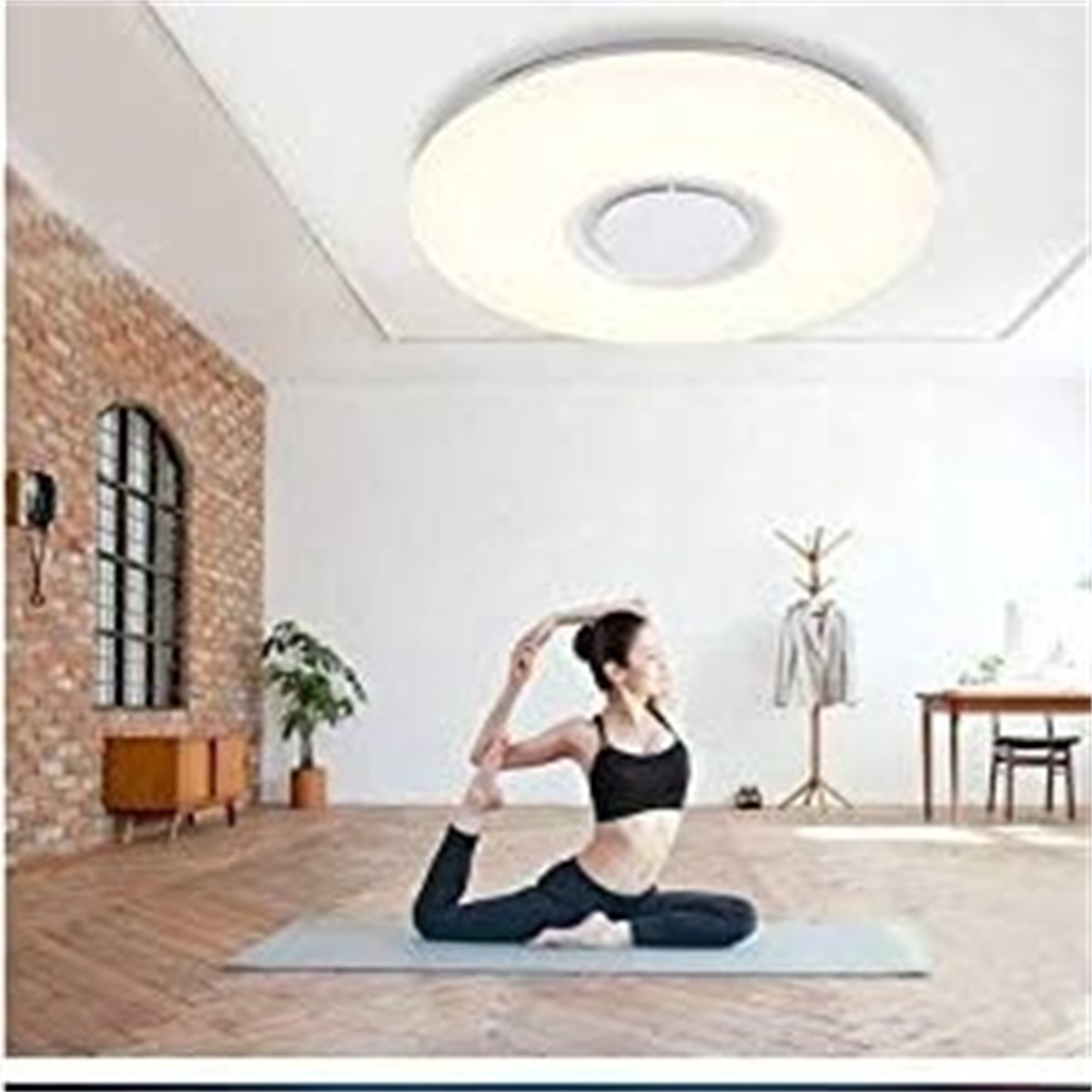 Frau macht Yoga unter Deckenleuchte. Ziegelwand und Fenster im Hintergrund.