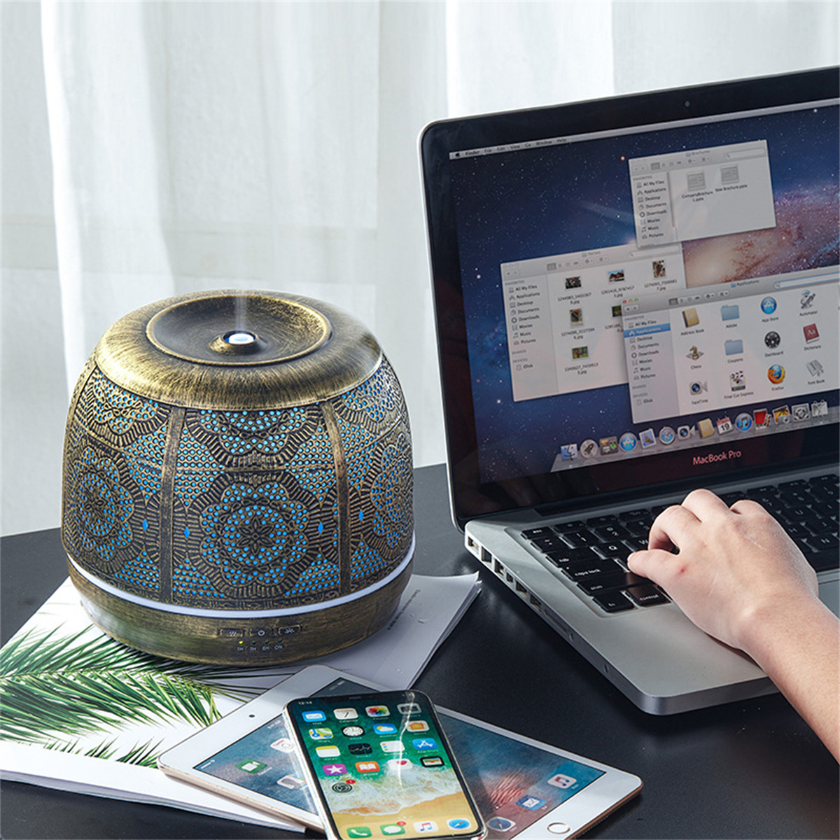 Ein Diffusor für ätherische Öle, ein Laptop, ein Tablet und ein Telefon stehen auf einem Schreibtisch. Eine Hand an der Tastatur.