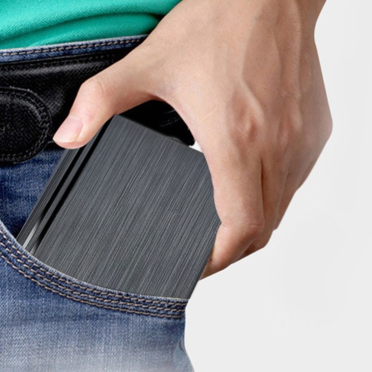 Hand in einer Tasche, die eine schwarze externe Festplatte hält. Jeans und Tasche sind sichtbar.
